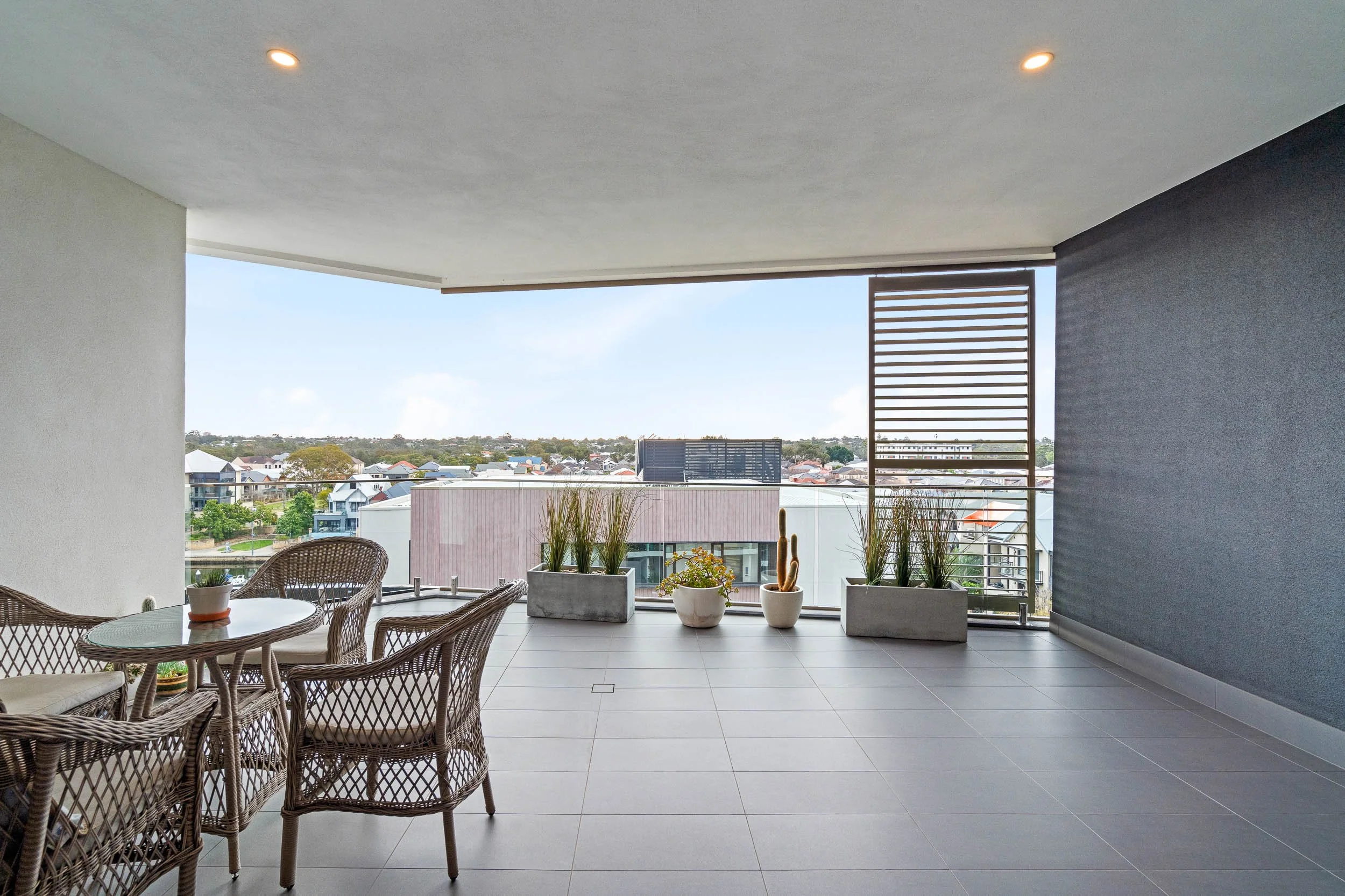 Spacious covered balcony with outdoor dining furniture, potted plants and neighbourhood views.