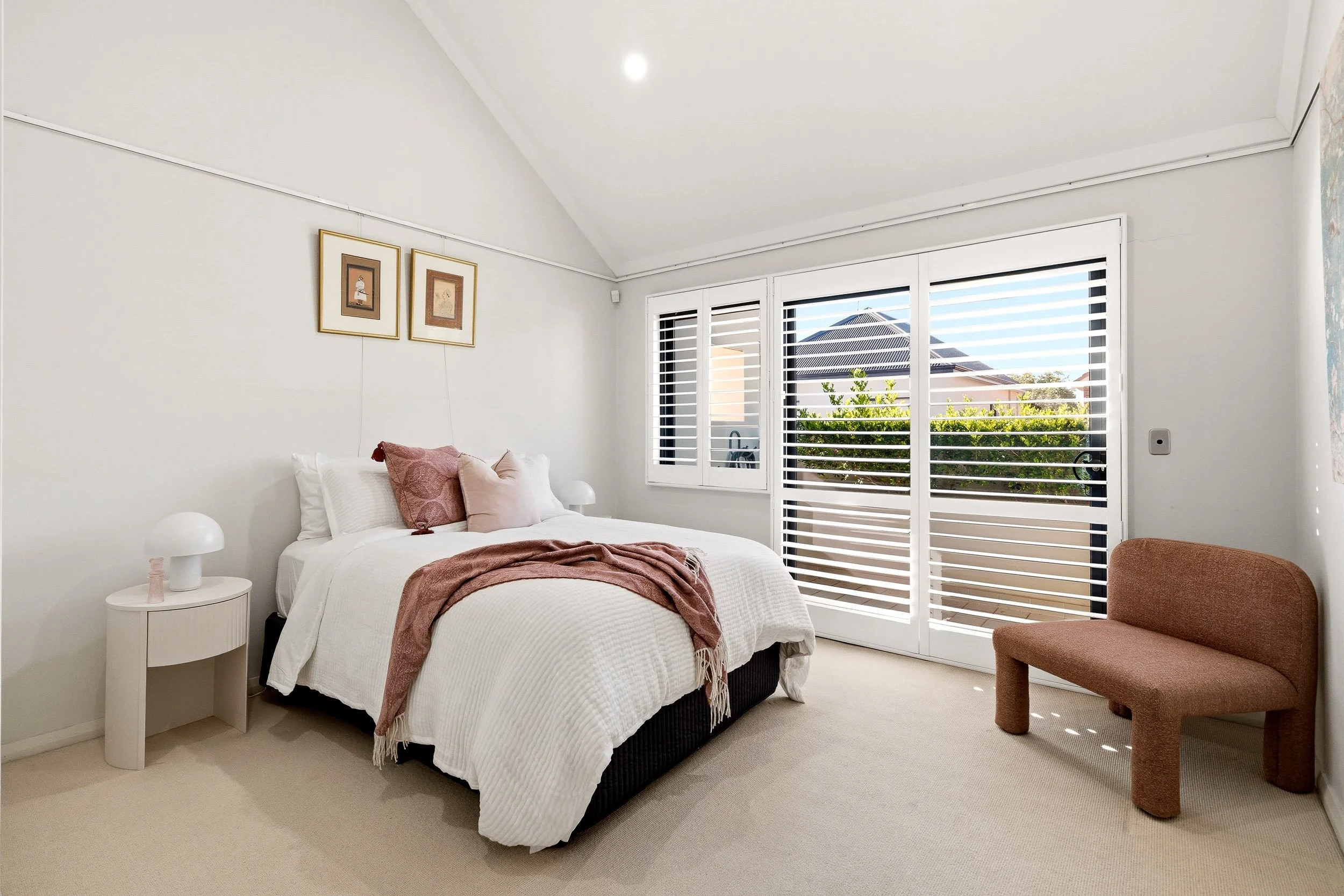 Bedroom with pink cushions, white shutters and soft daylight.