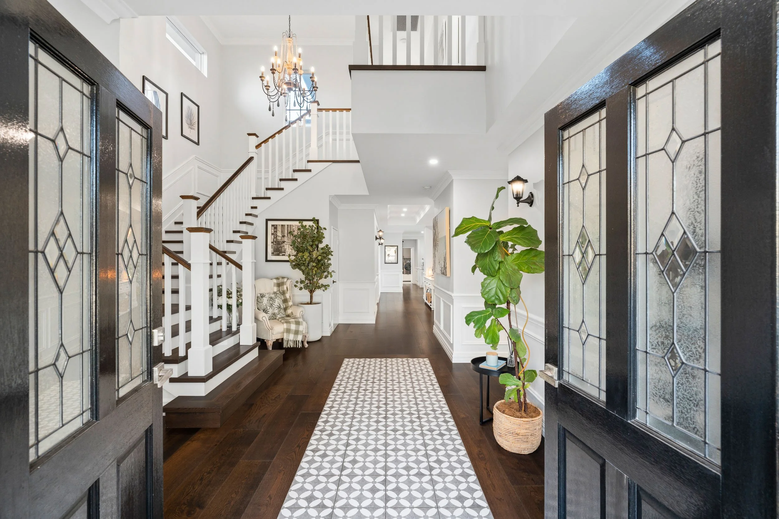 Entrance hall with leadlight double doors, dark timber floors and a white staircase beneath a chandelier.