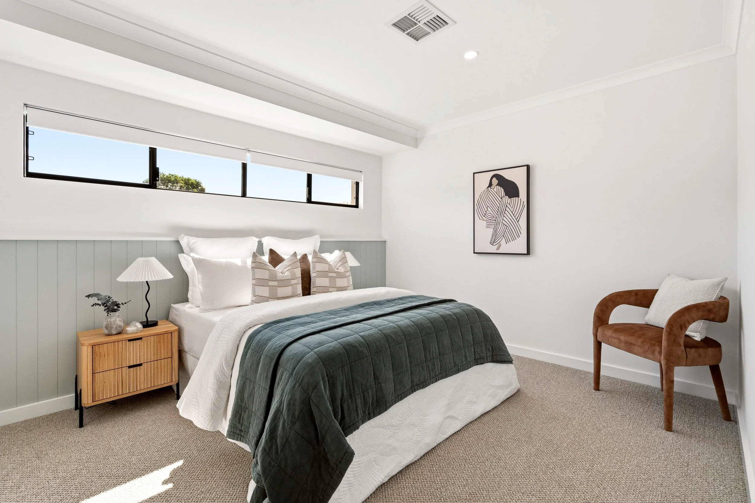 Bedroom with a teal bedspread, textured rug and a high horizontal window.