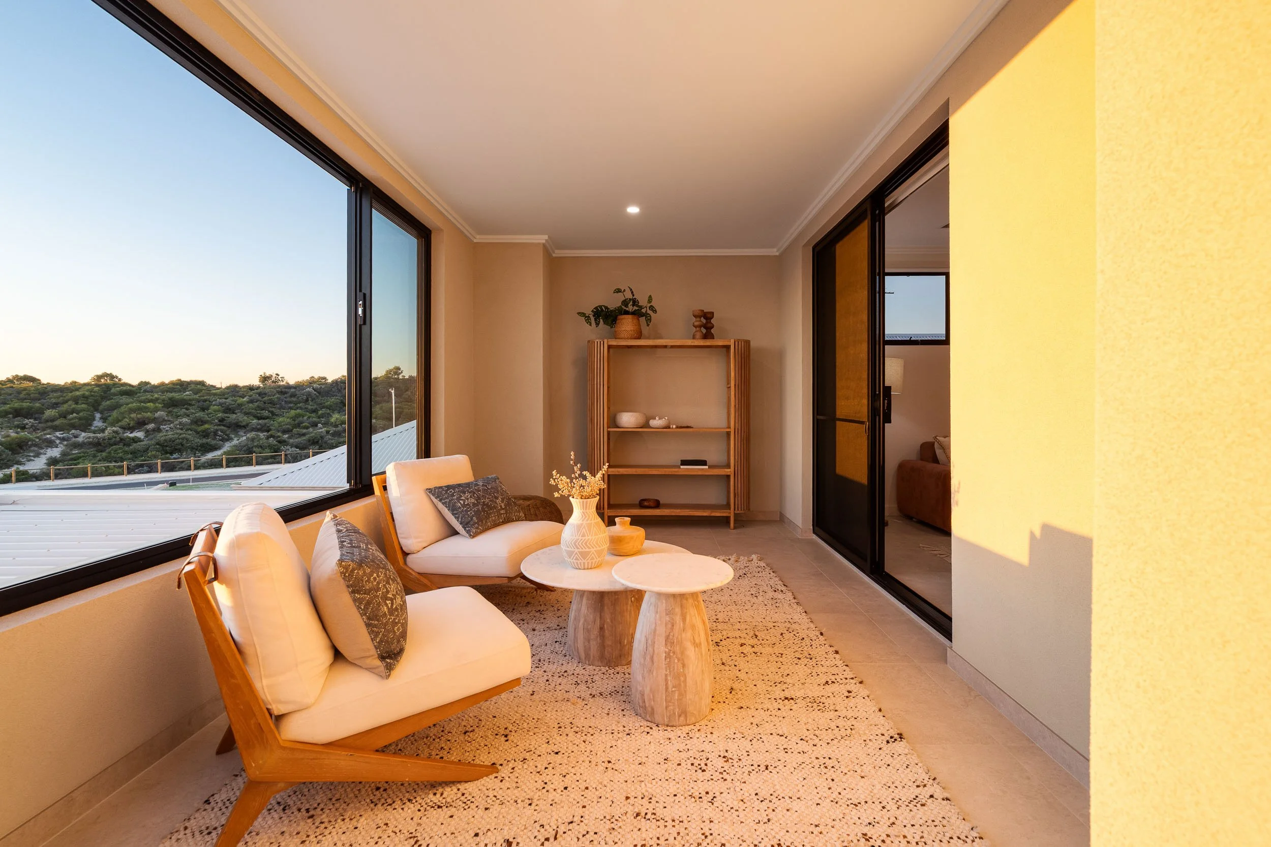 Sunroom with timber-framed lounge chairs, a textured rug and large windows catching the evening light.