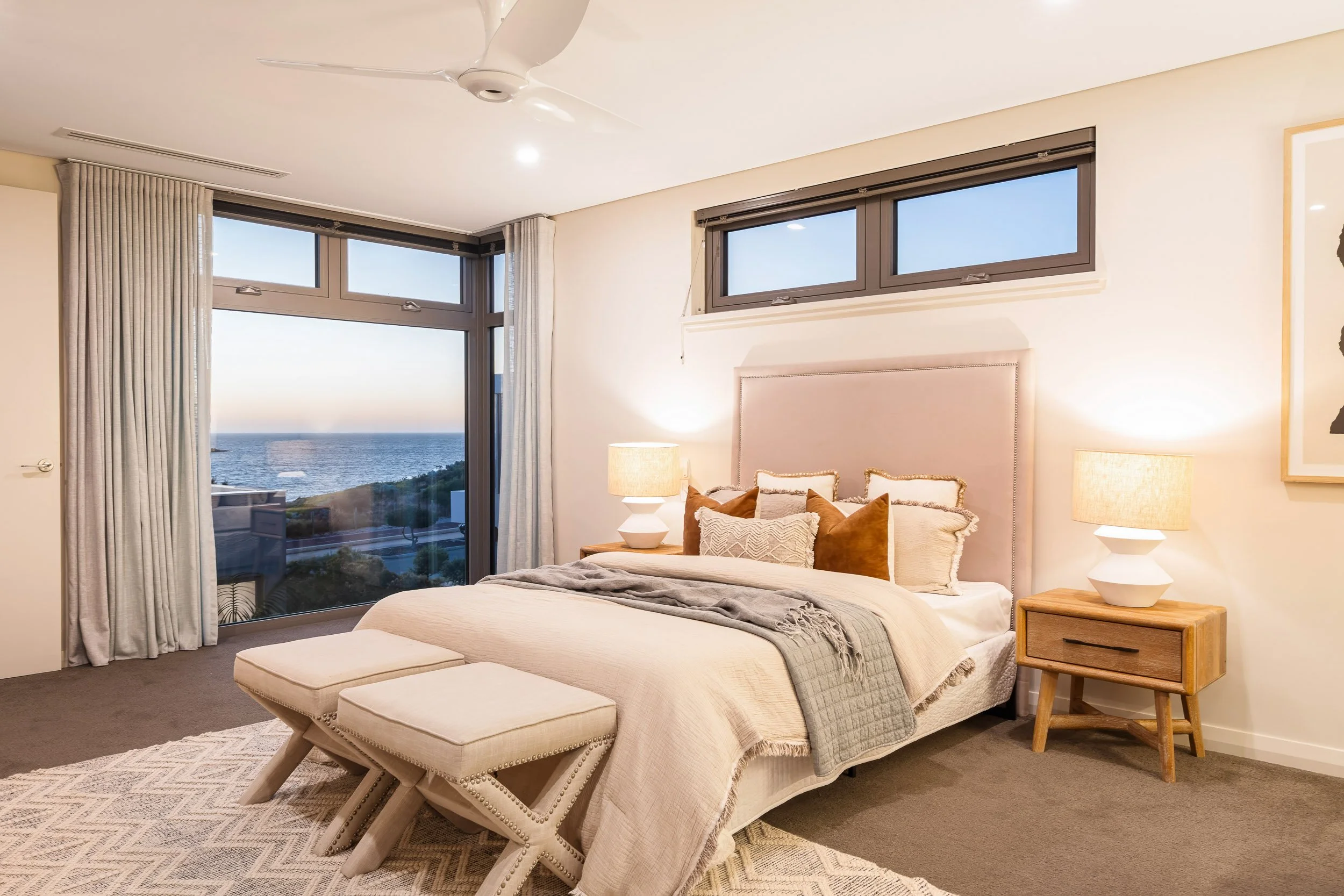 Bedroom with high windows, a textured feature wall and a bench at the foot of the bed.