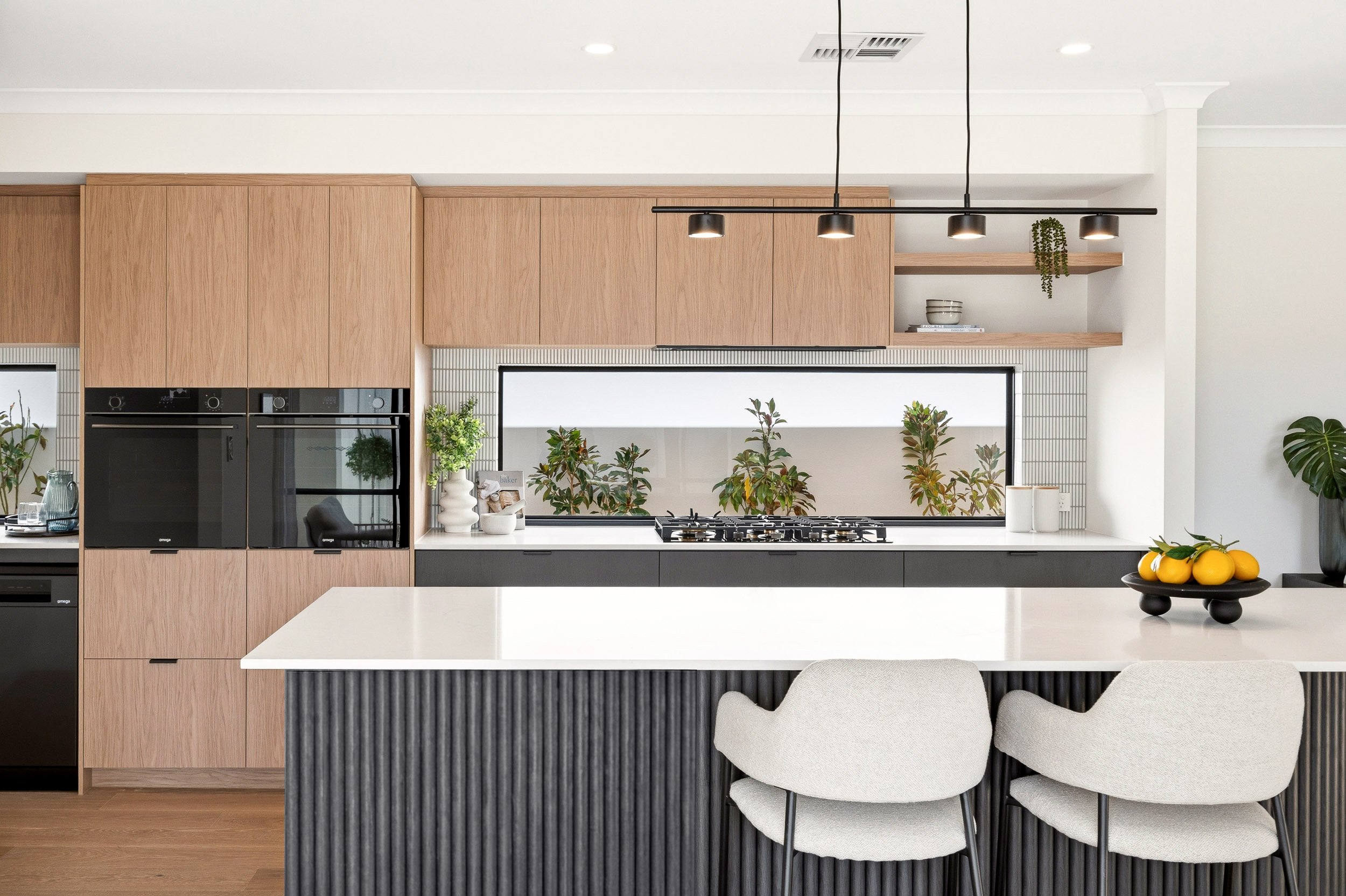 Kitchen with timber overhead cabinets, a dark fluted island and white bar stools.