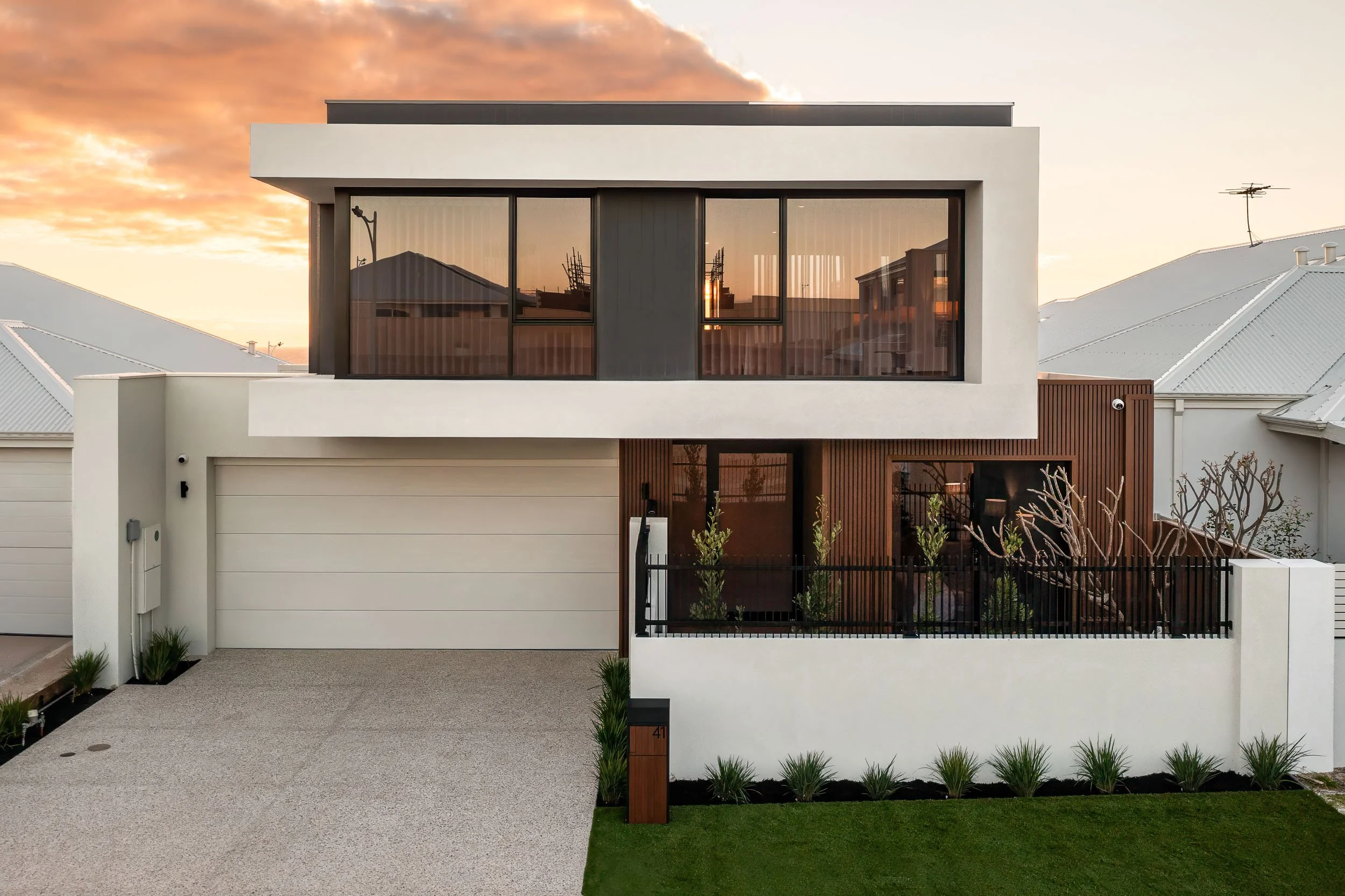 Contemporary two-storey home at sunset with broad black-framed windows and an integrated garage.