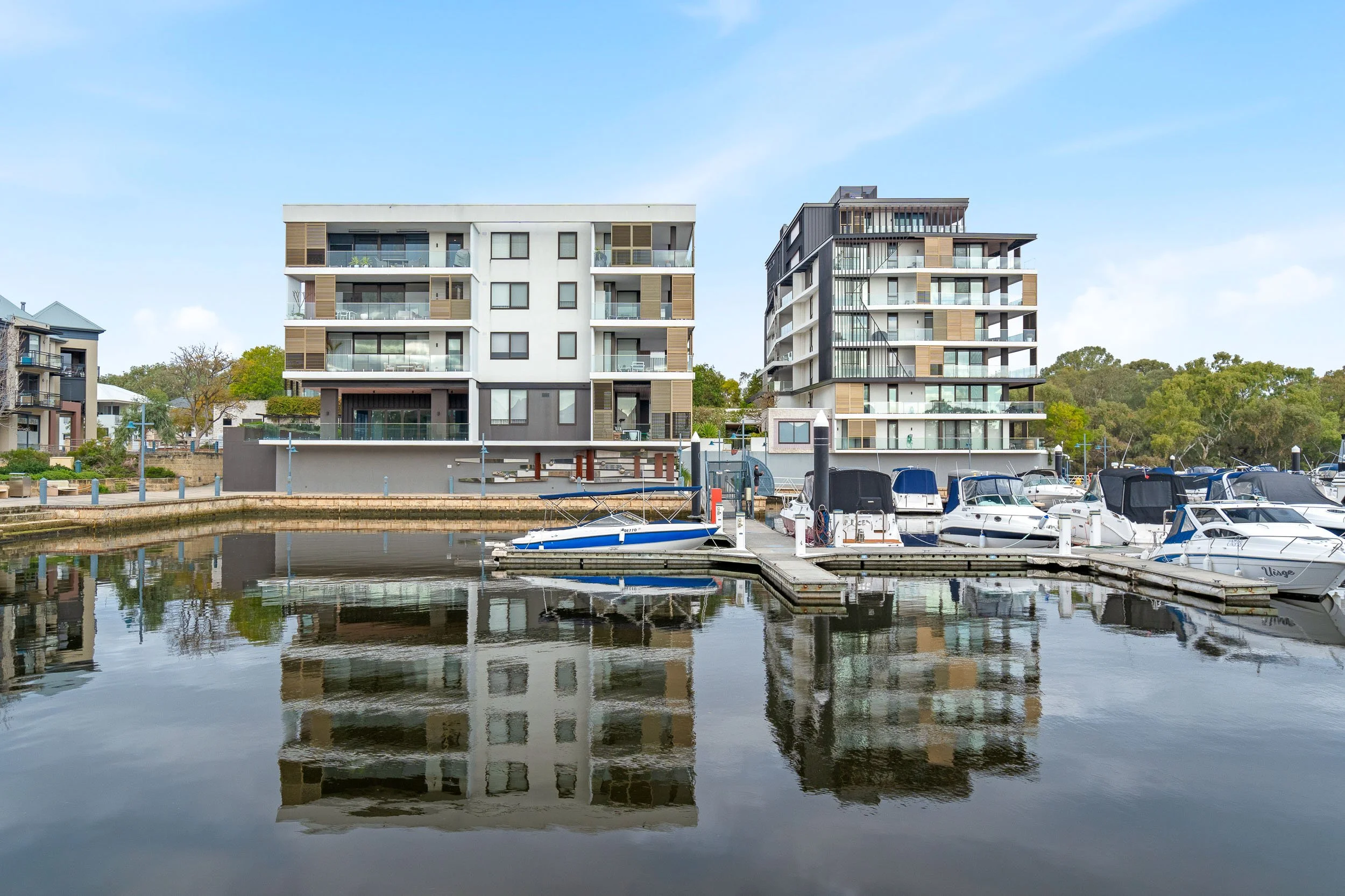 Waterfront apartments and moored boats reflected in a sheltered marina.