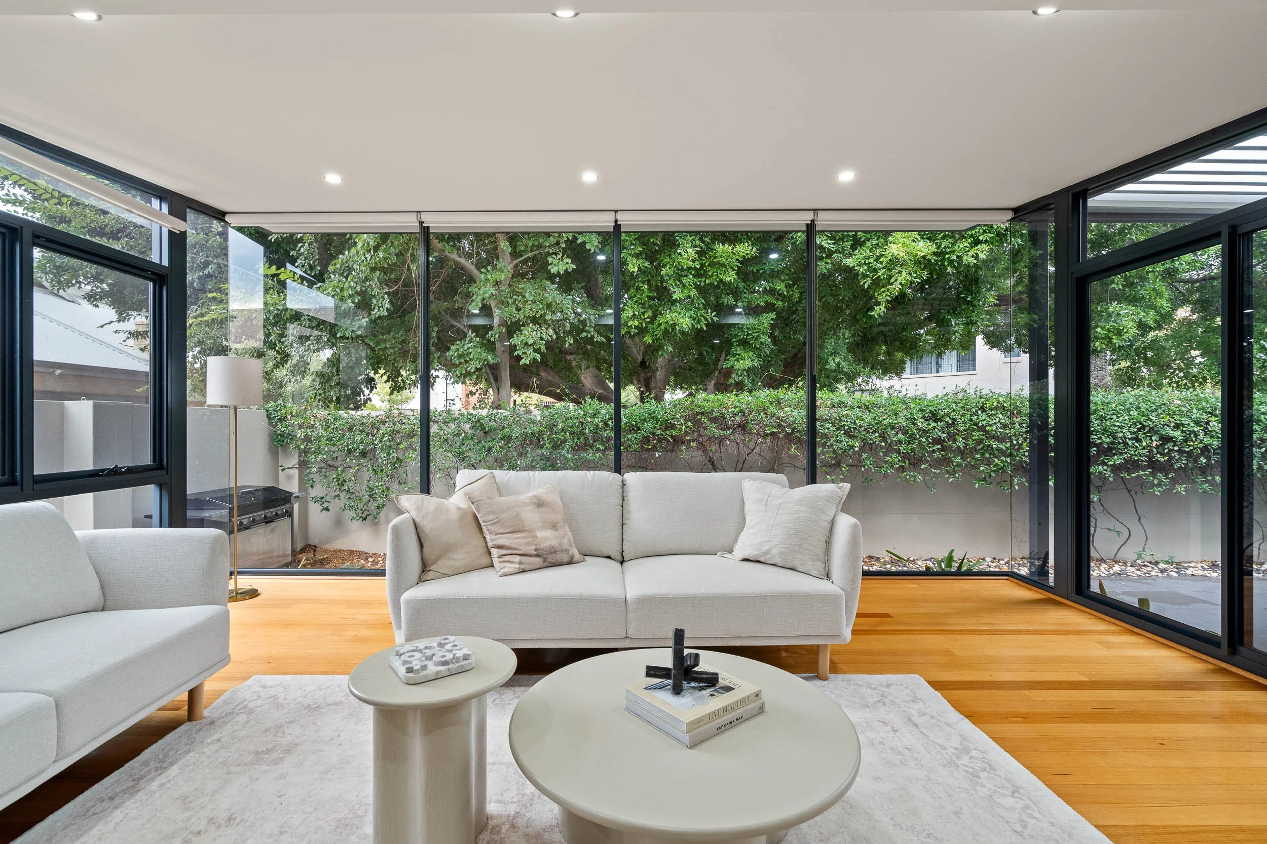 Living room with a curved pale sofa and expansive windows overlooking trees.