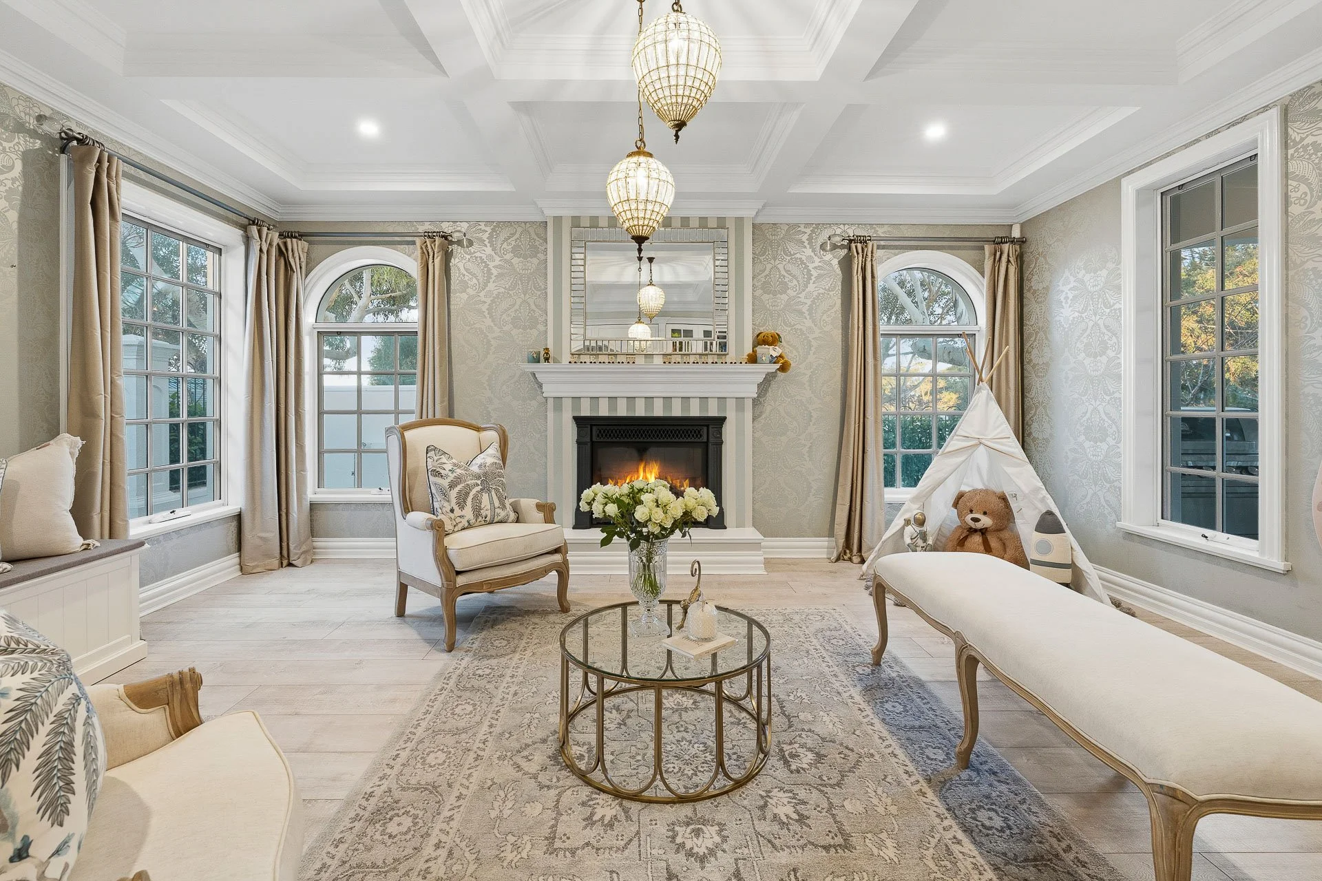 Formal living room with a fireplace, chandelier, upholstered seating and a patterned rug.