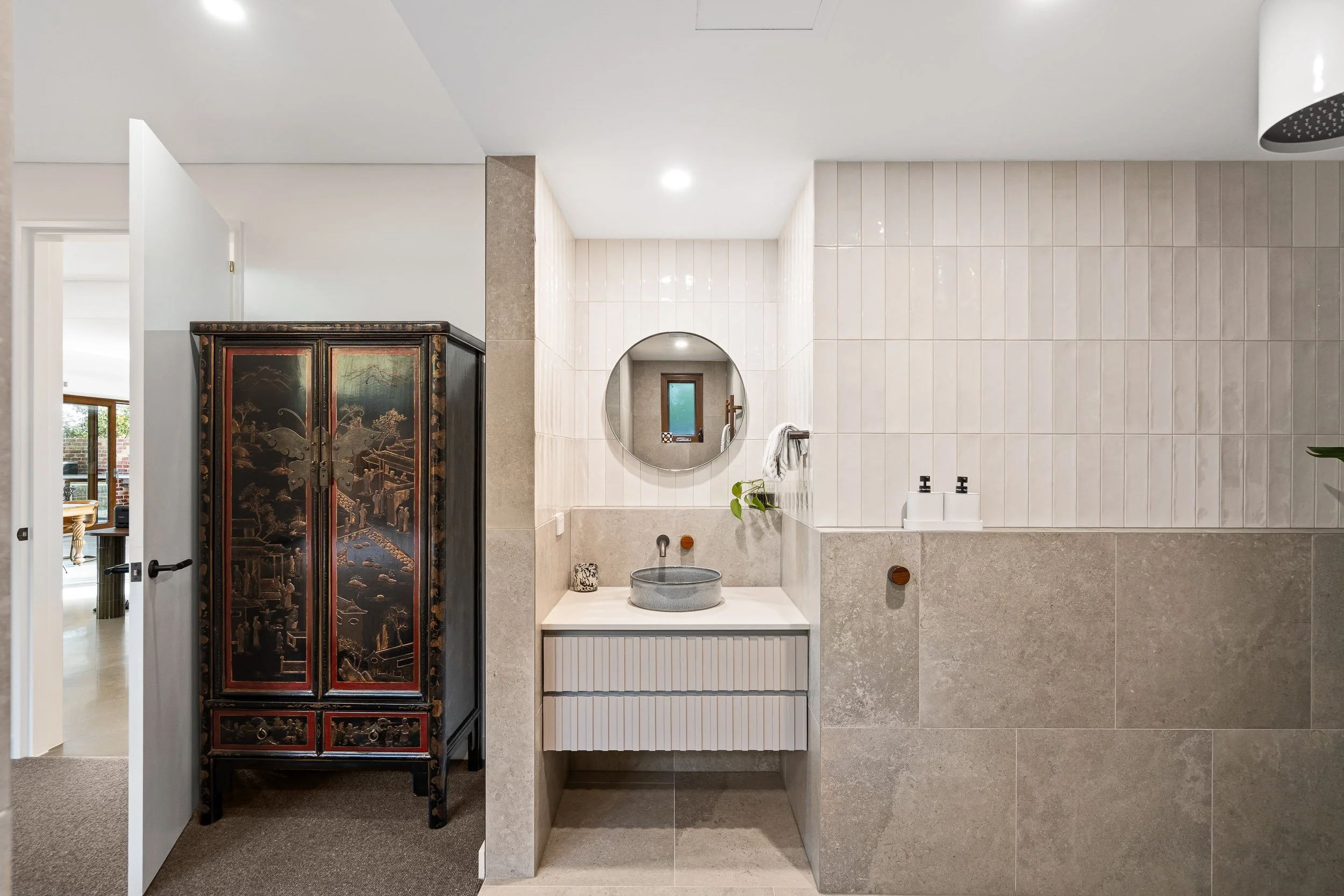 Bathroom with a white vanity, a rounded mirror and light textured finishes.