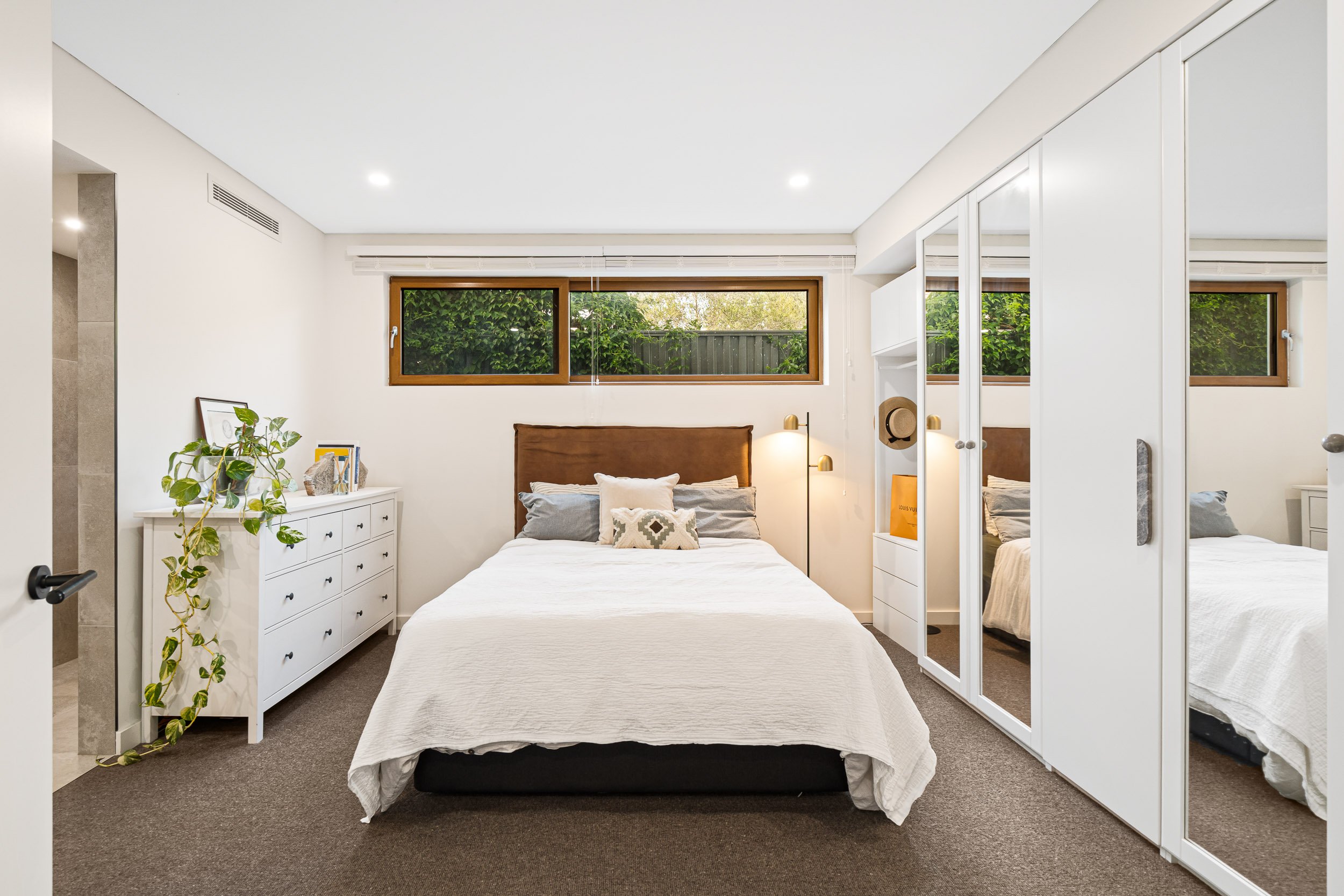 Bedroom with a white bedspread, textured walls and a high window overlooking greenery.