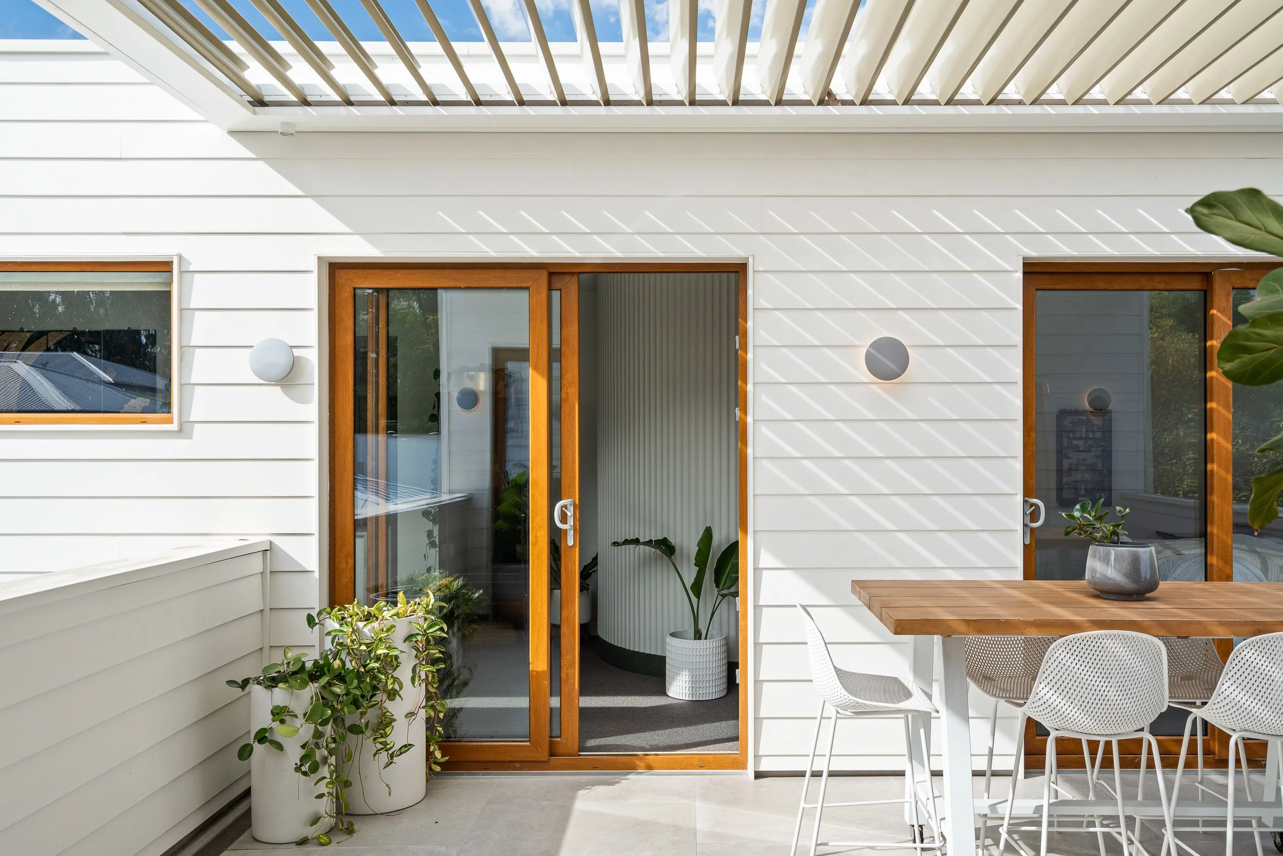 Covered timber deck with an outdoor dining setting and sliding timber-framed doors.