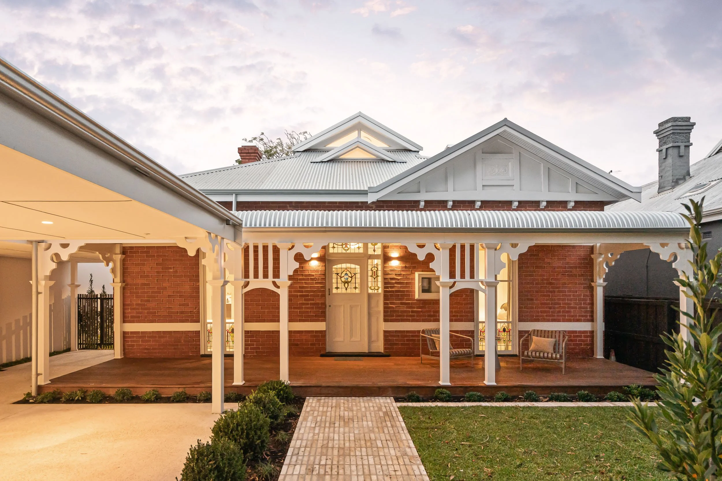 Traditional red-brick home with a decorative white veranda and a paved path through the front garden.