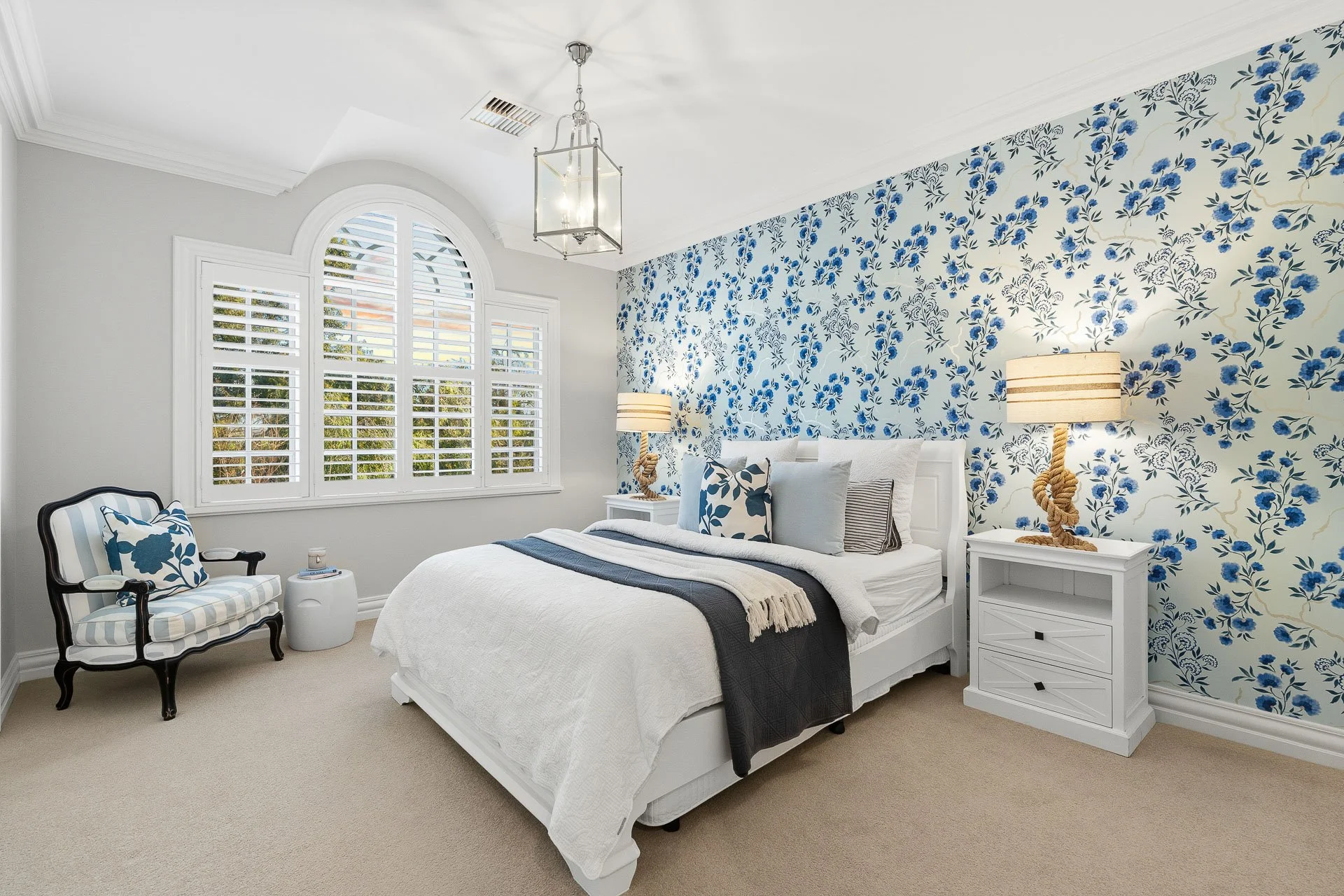 Bedroom with a blue patterned feature wall, arched window and chandelier.