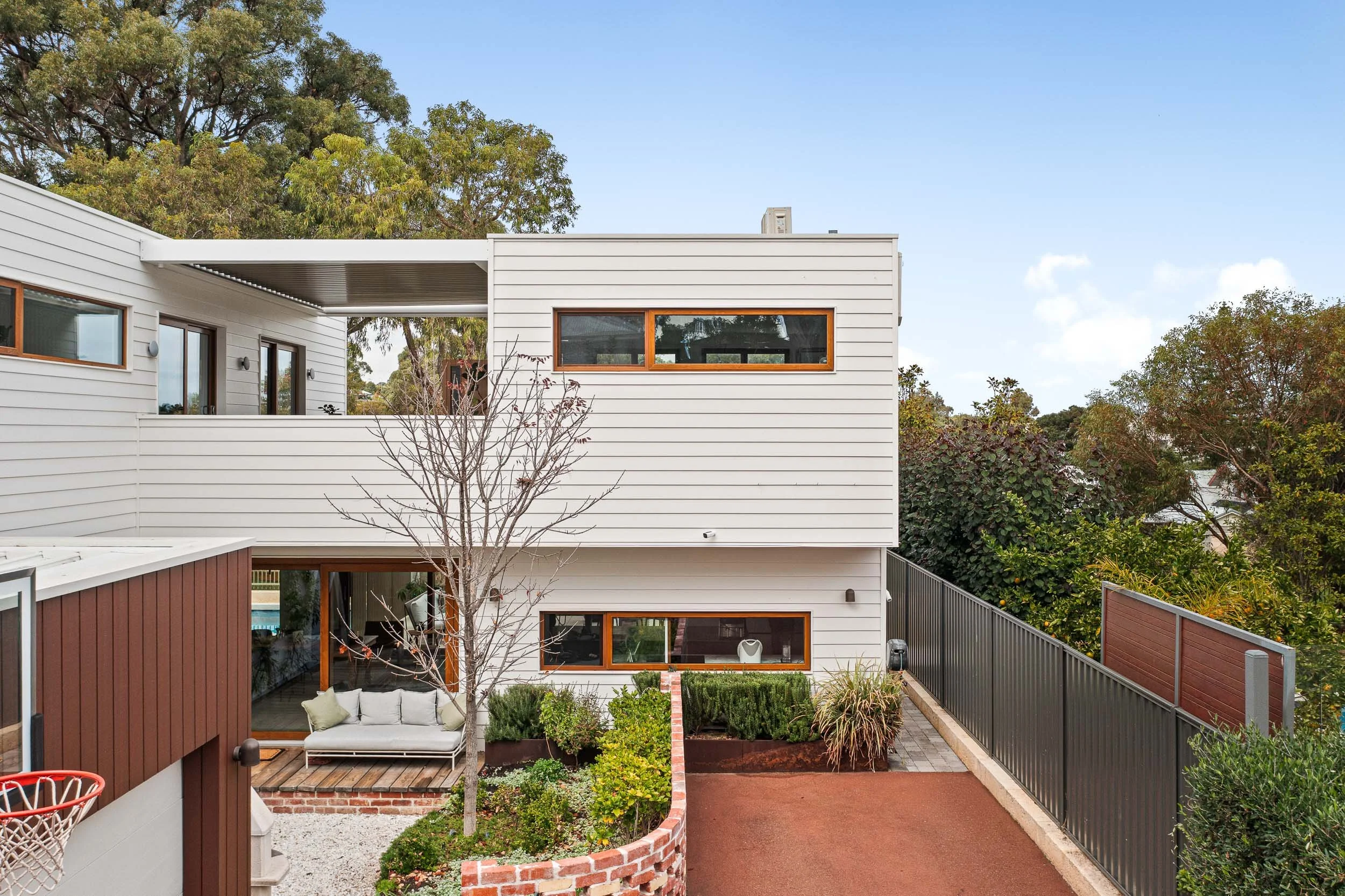 Two-storey white-clad home overlooking a brick-paved courtyard with a central tree.