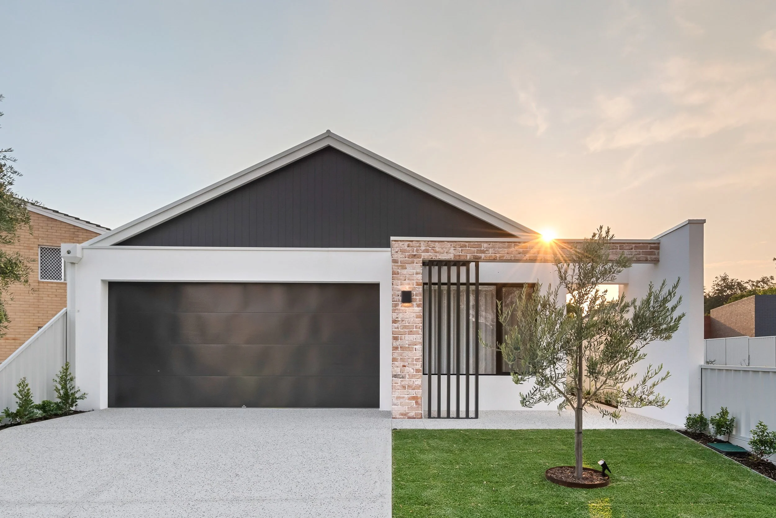 Single-storey gabled home at sunset with a dark garage door and illuminated landscaping.