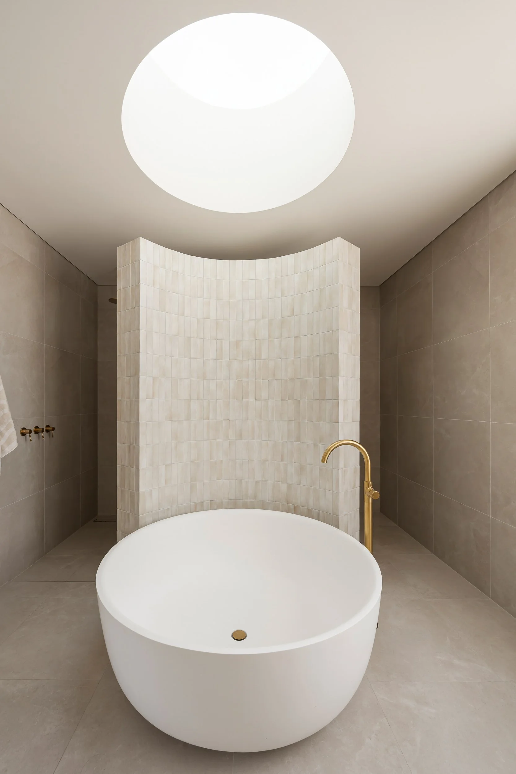 Bathroom with a freestanding oval bath, curved tiled screen and circular skylight.