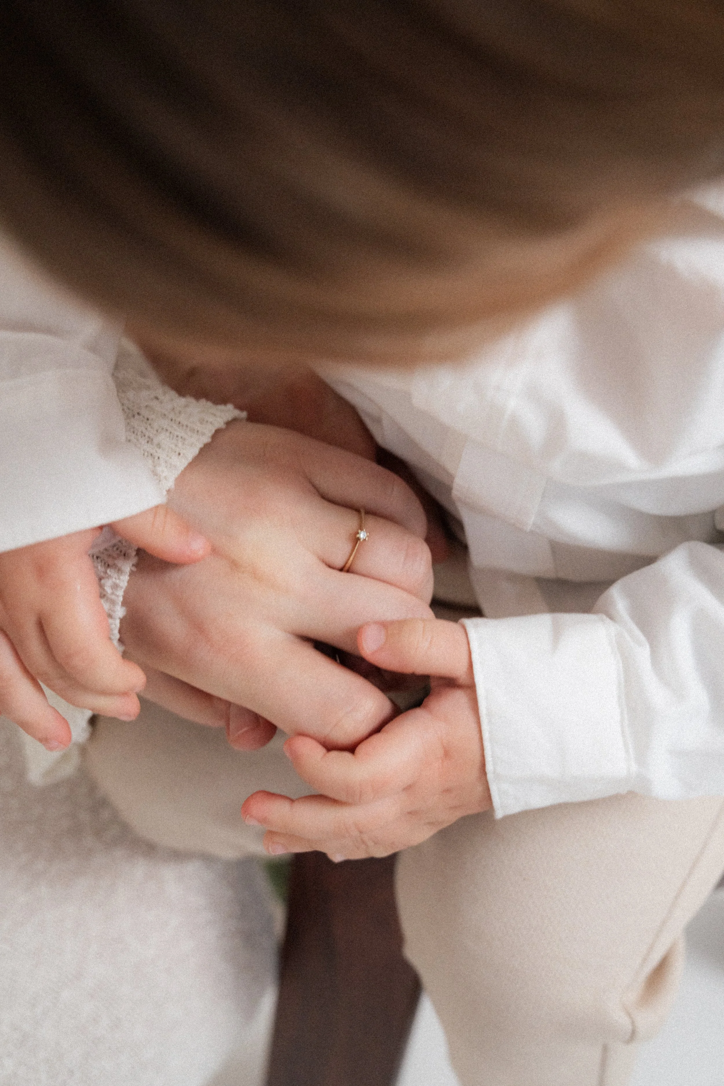 Close-up of a woman and a child's hands, the woman wearing a ring, holding hands gently.