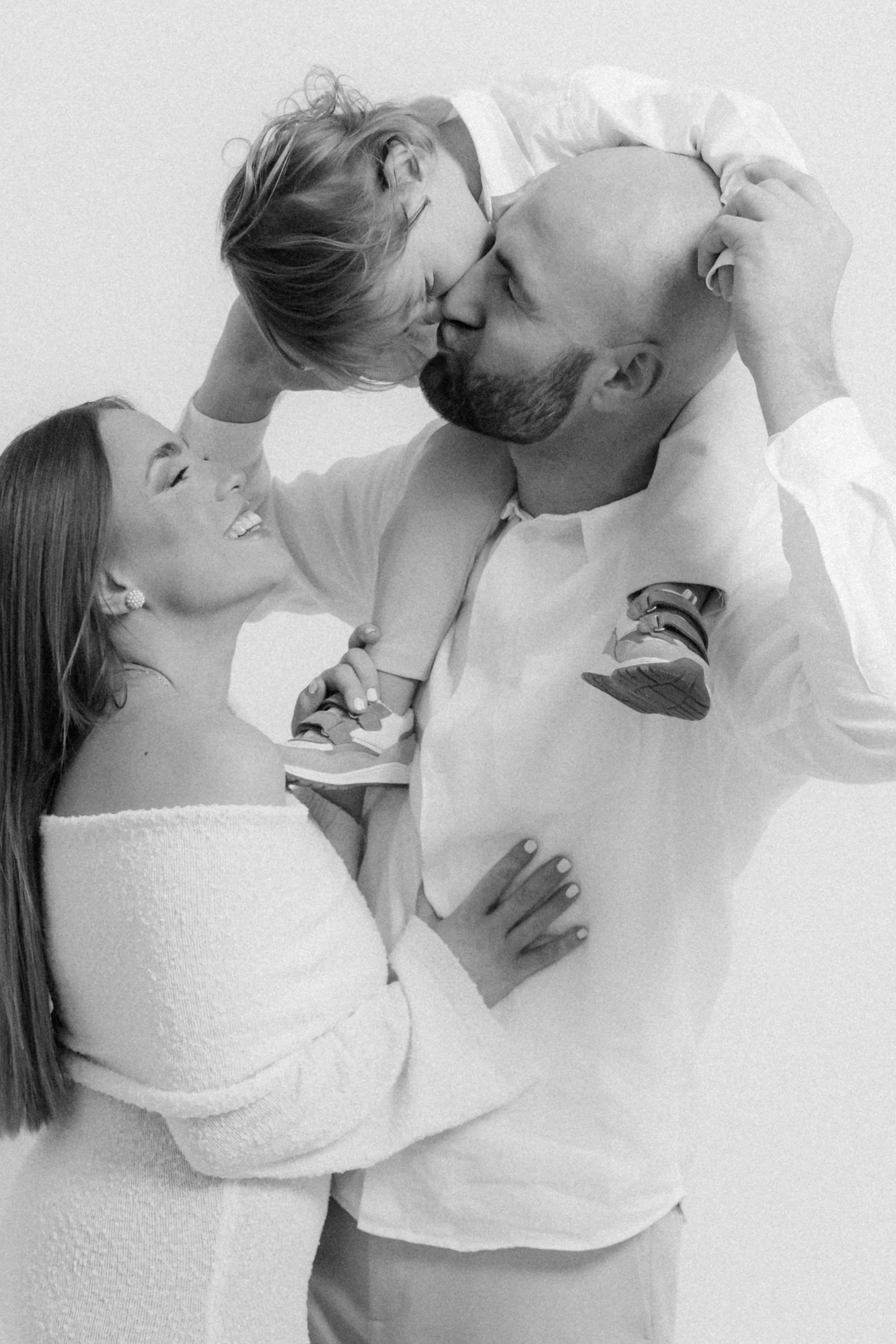 Family of three celebrating with a kiss, father holding a young boy, mother smiling and touching father's chest