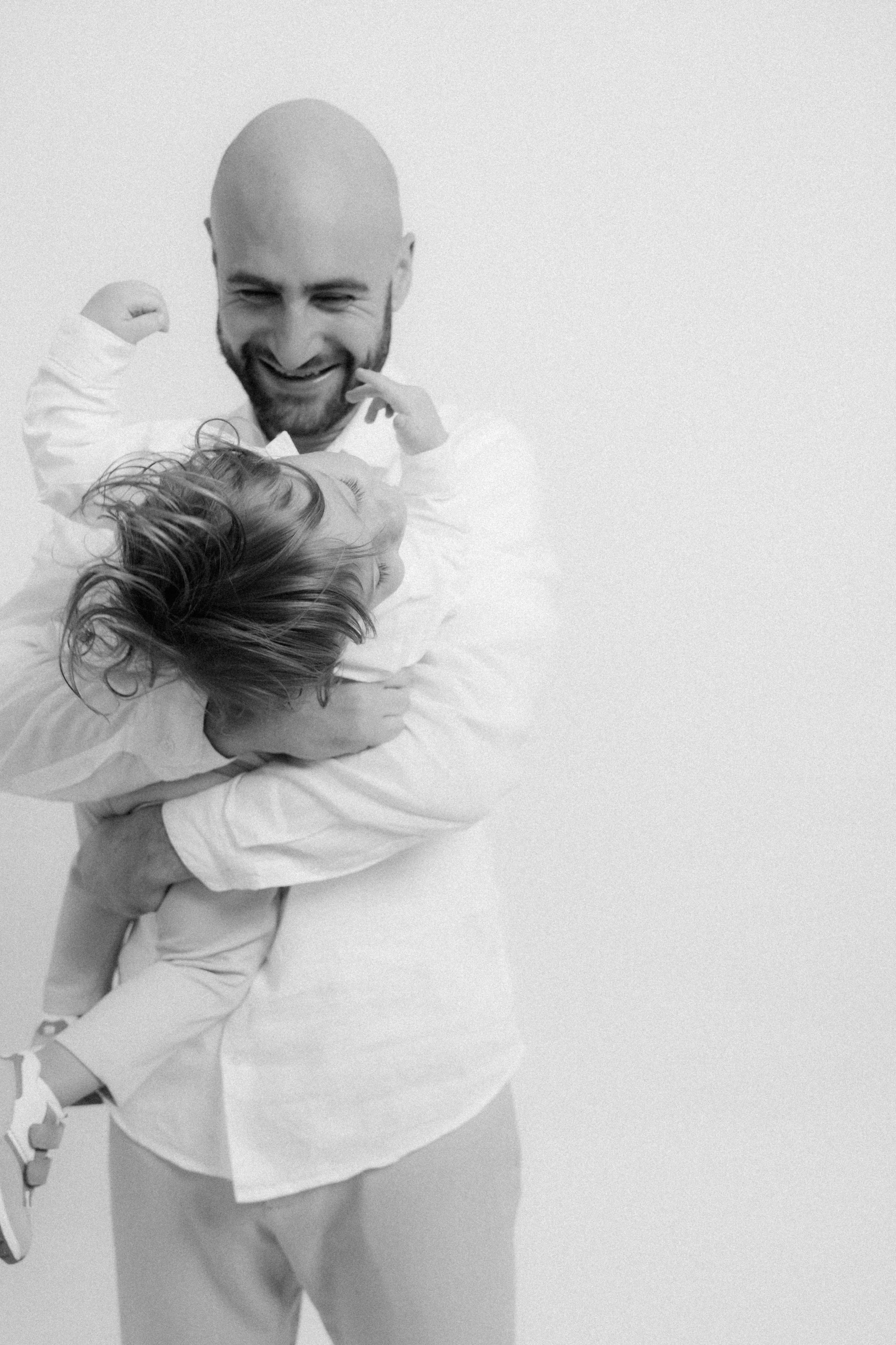 A man lifting a child in an embrace, both smiling and appearing happy.