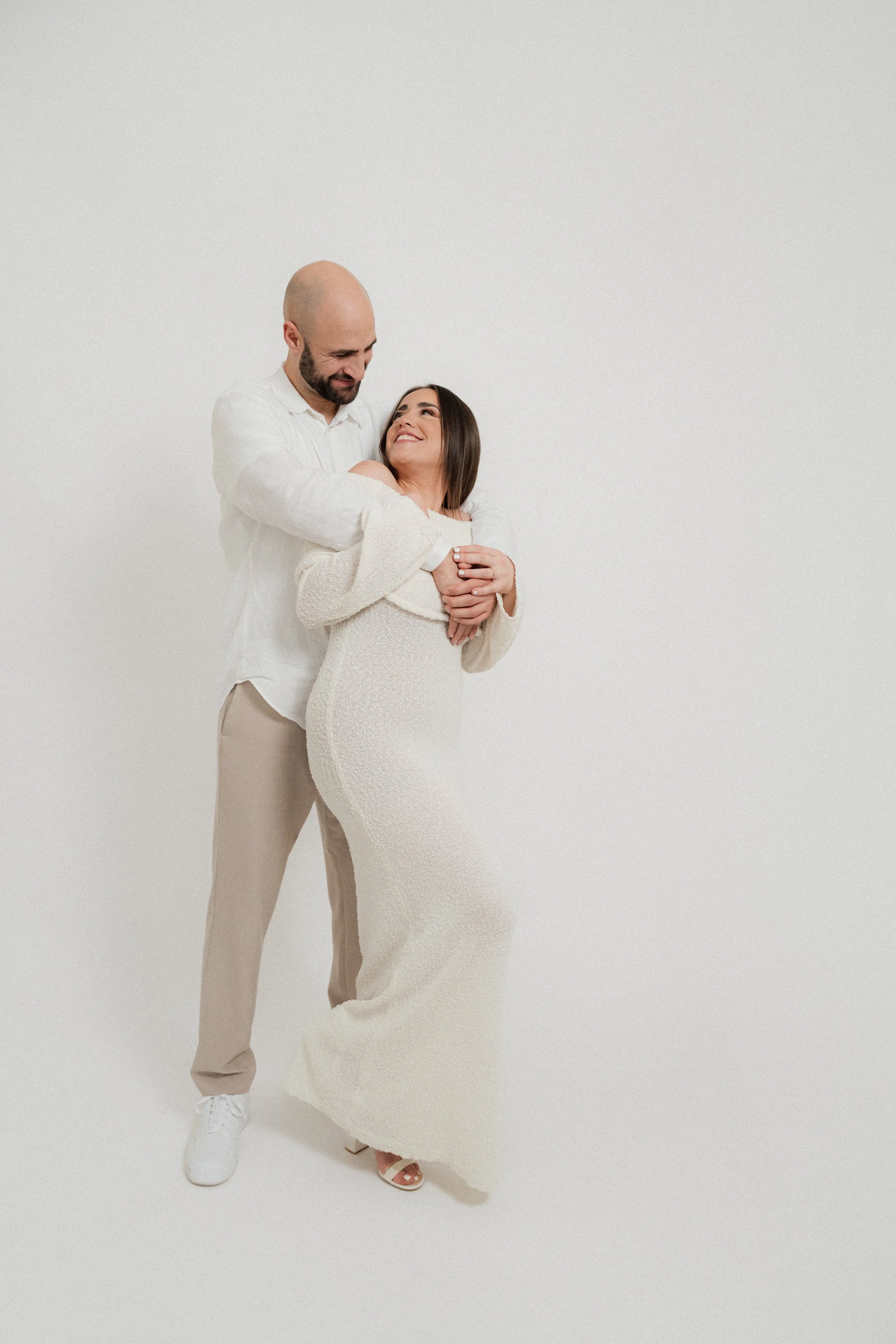 A man and woman smiling and embracing each other in a white studio.