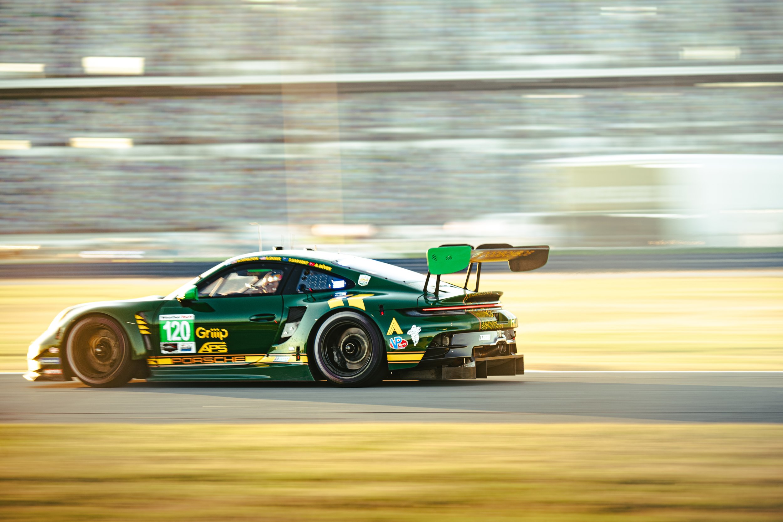 Green Porsche race car on a track, moving at high speed with blurred background.