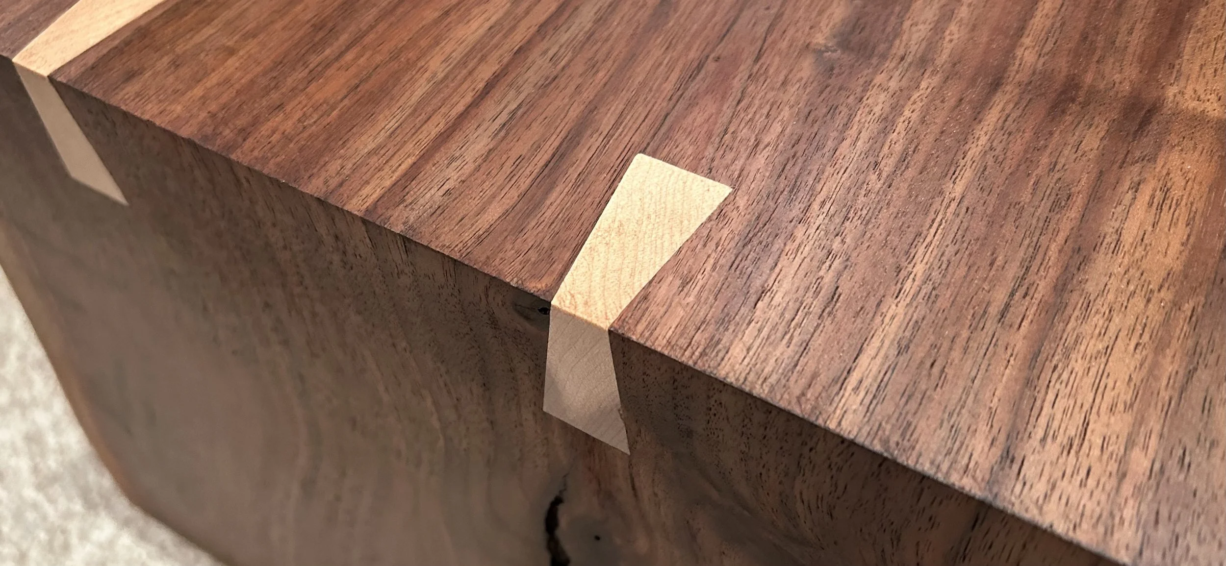 Close-up of a wooden furniture corner with a small light-colored wood inlay in the joint.