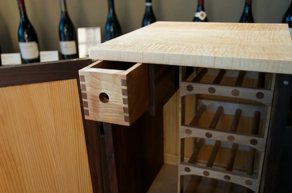 Wooden furniture with shelves, drawer, and wine bottles in the background.