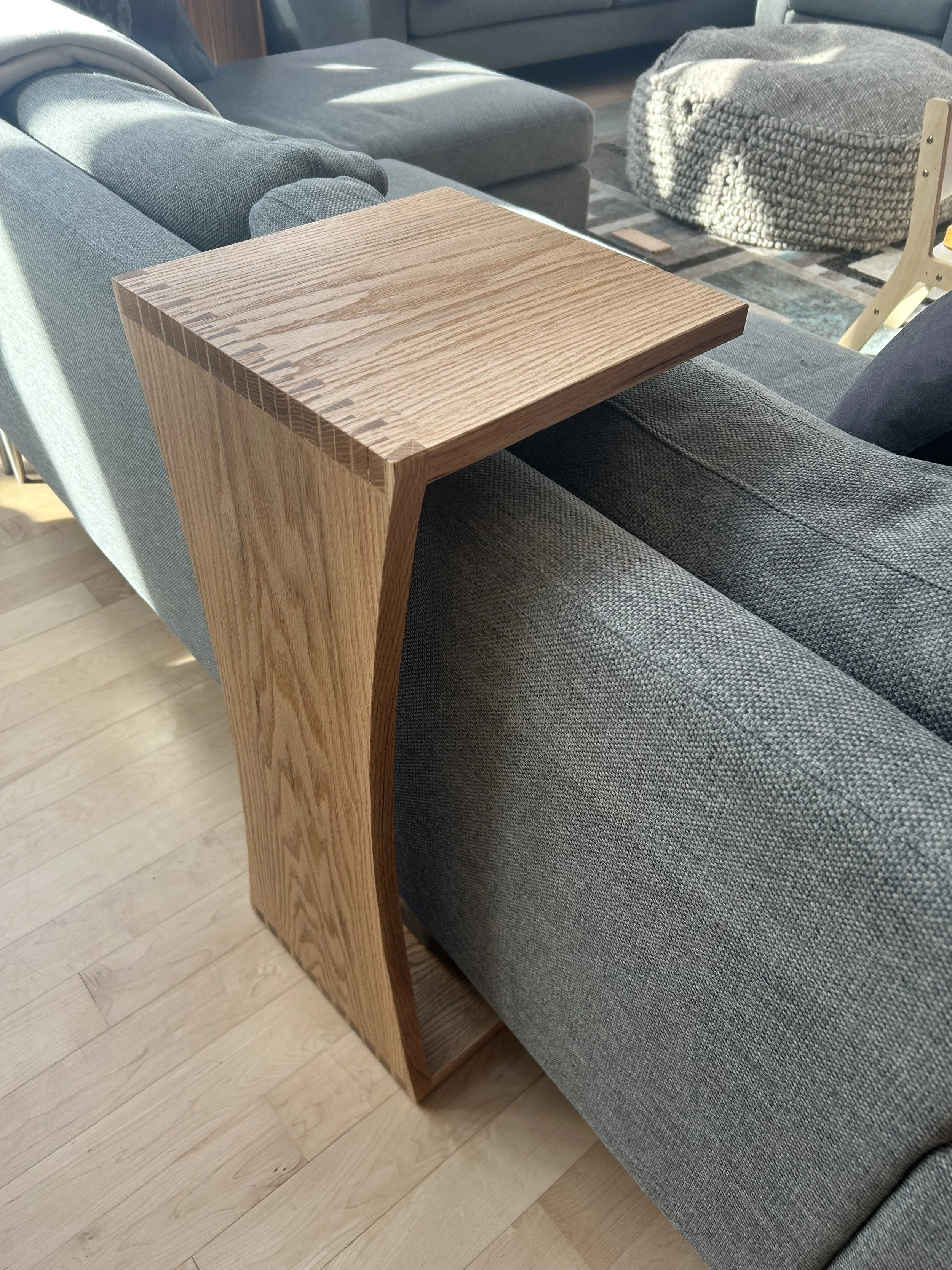A wooden side table with a curved side panel placed between two gray upholstered sofas in a living room.