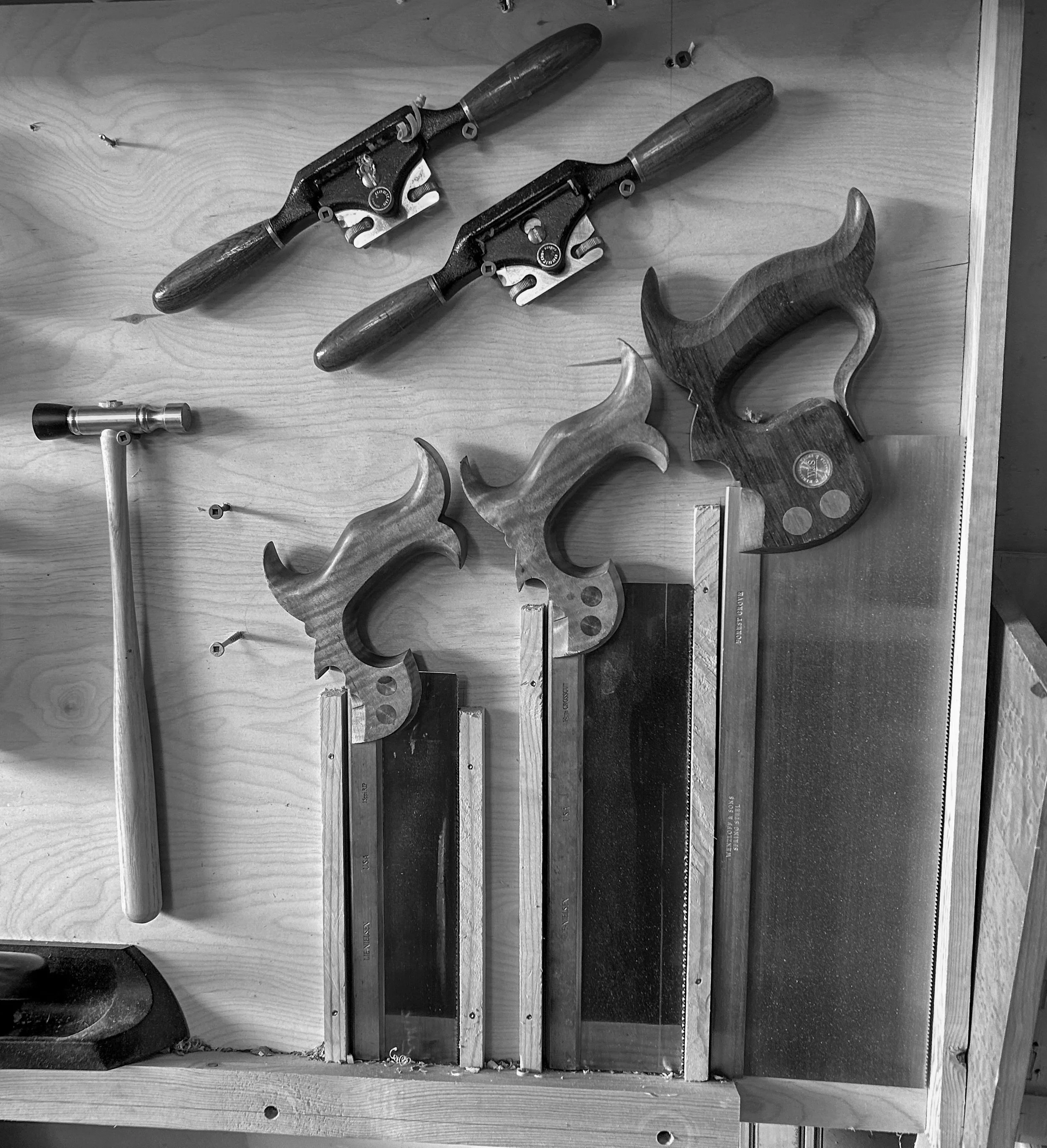 Three saw blades with curved handles, a small hammer, two hand saws with wooden handles, and a metal square on a wooden workbench.