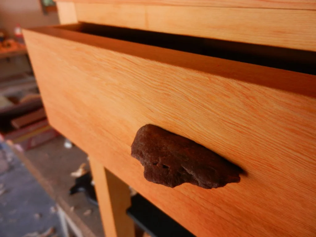 Close-up of a wooden drawer with a dark, irregularly shaped rock attached to the front handle.