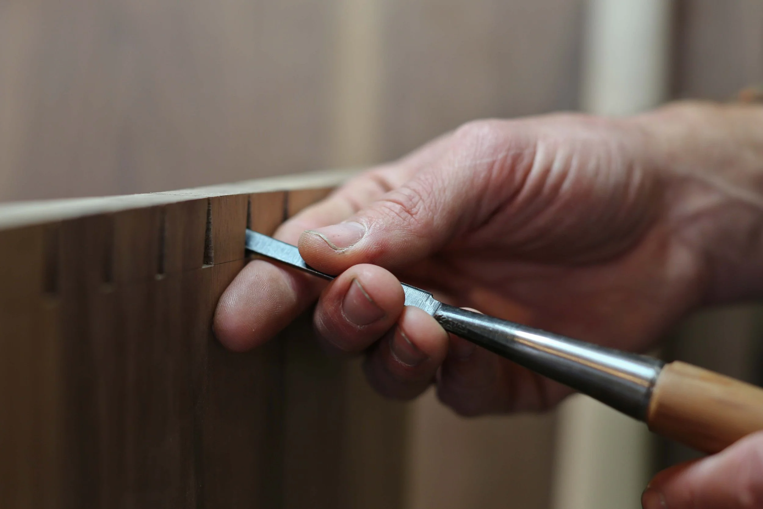 Close-up of a person's hand using a chisel to carving or shaping a piece of wood.