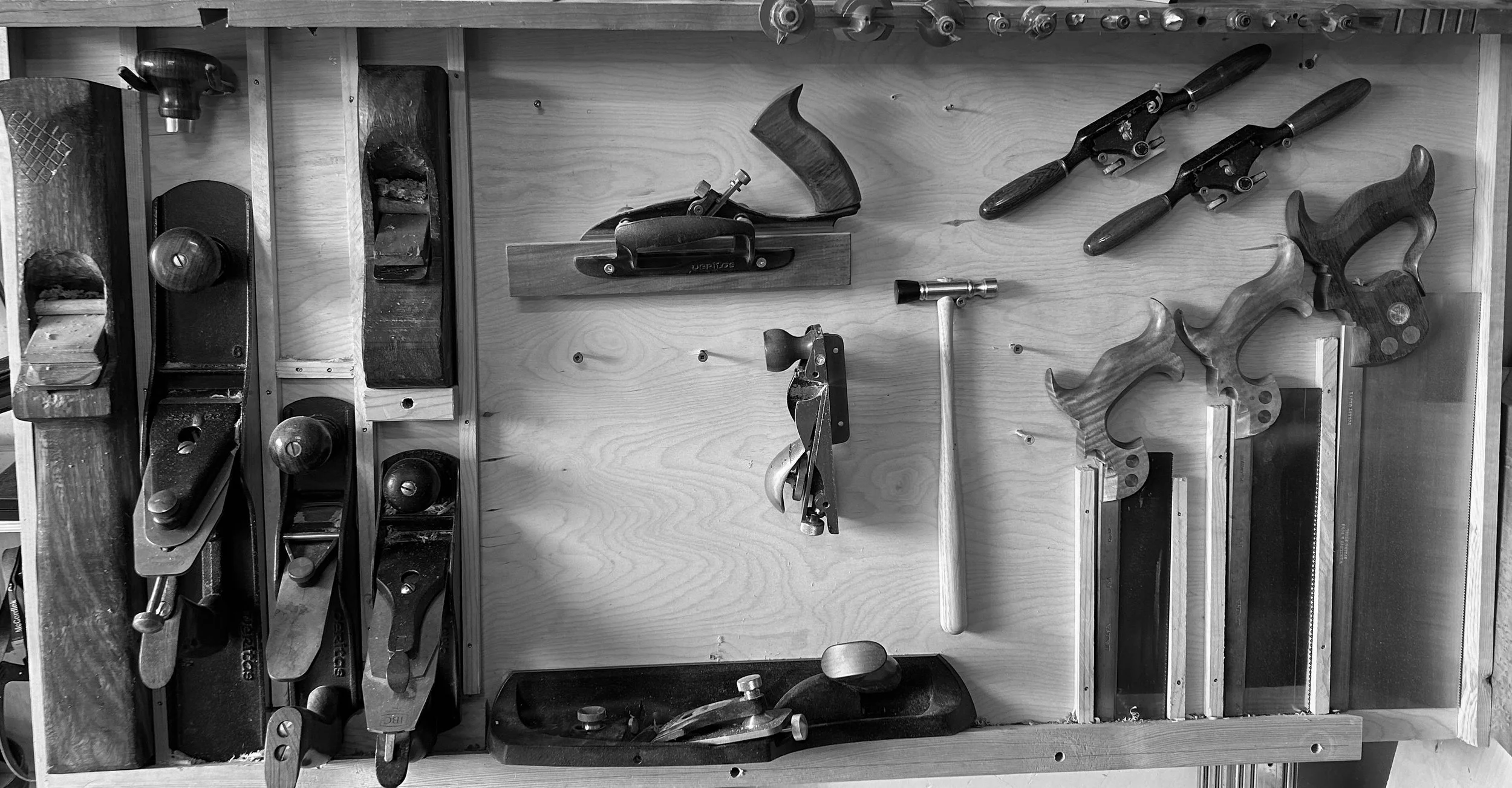 Assorted woodworking hand tools arranged on a workbench, including hand planes, saws, a hammer, and clamps.