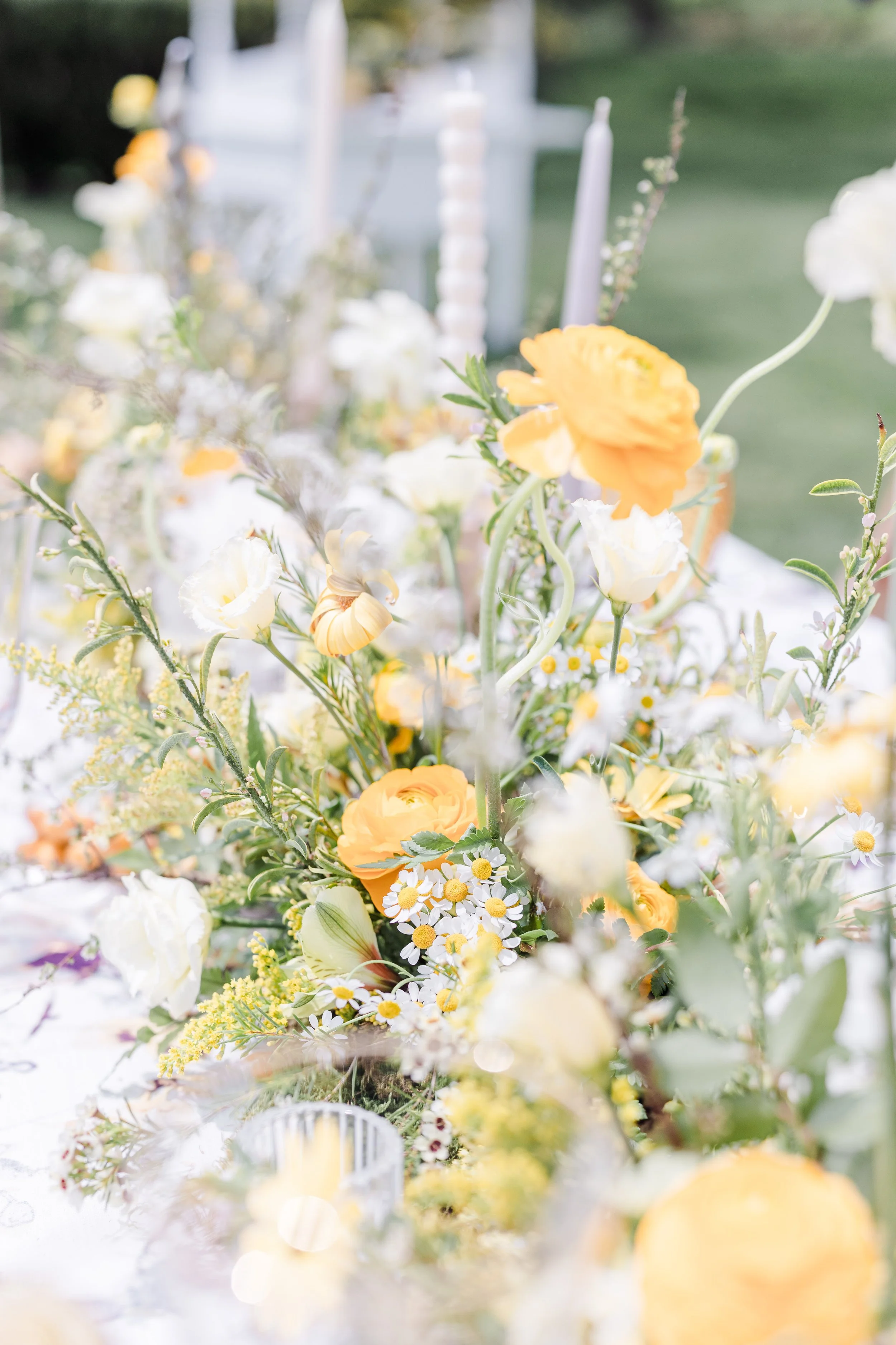 A floral arrangement with yellow, white, and green flowers, set on a white table outdoors.