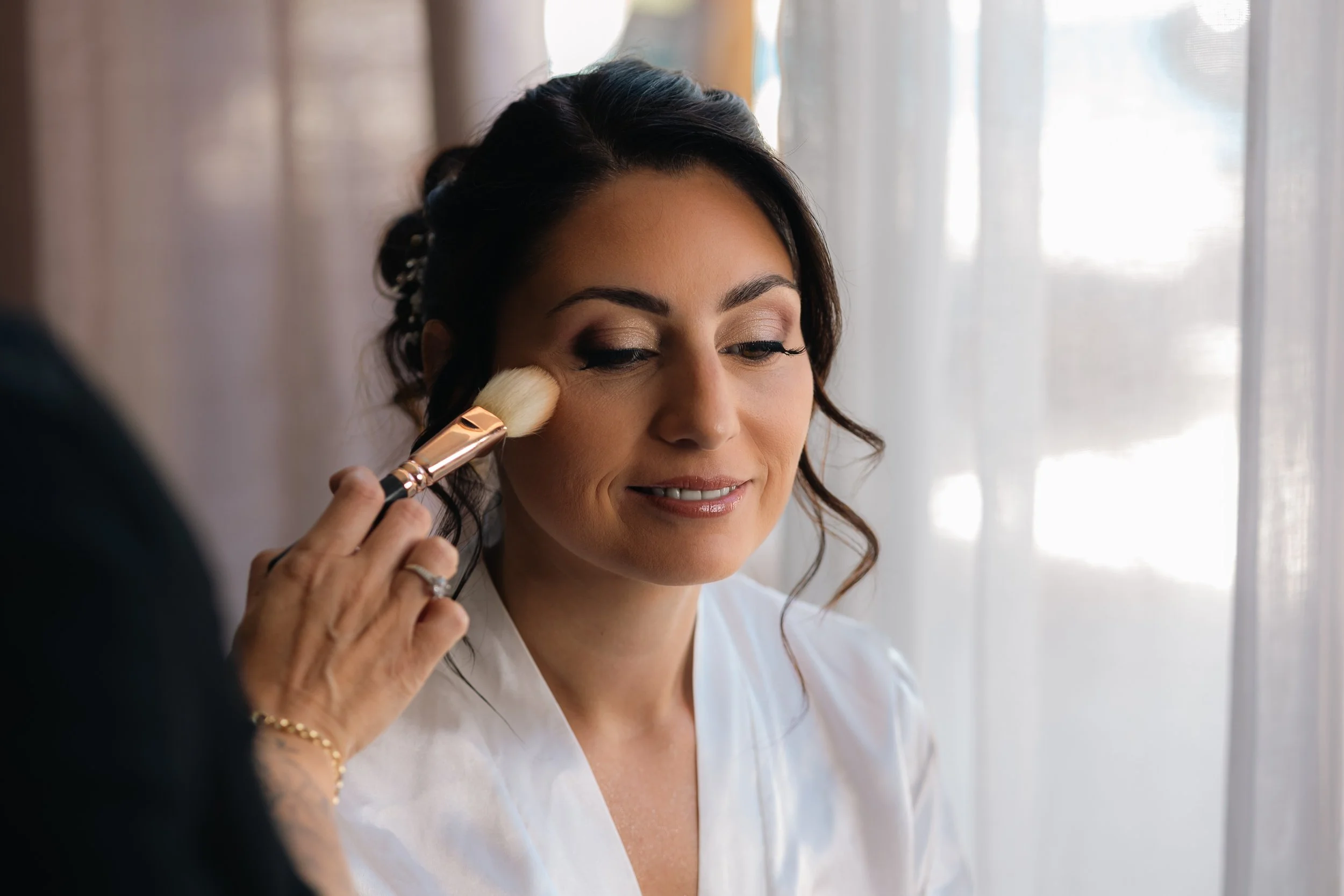 Une femme reçoit un maquillage au visage, une autre personne applique du maquillage avec un pinceau
