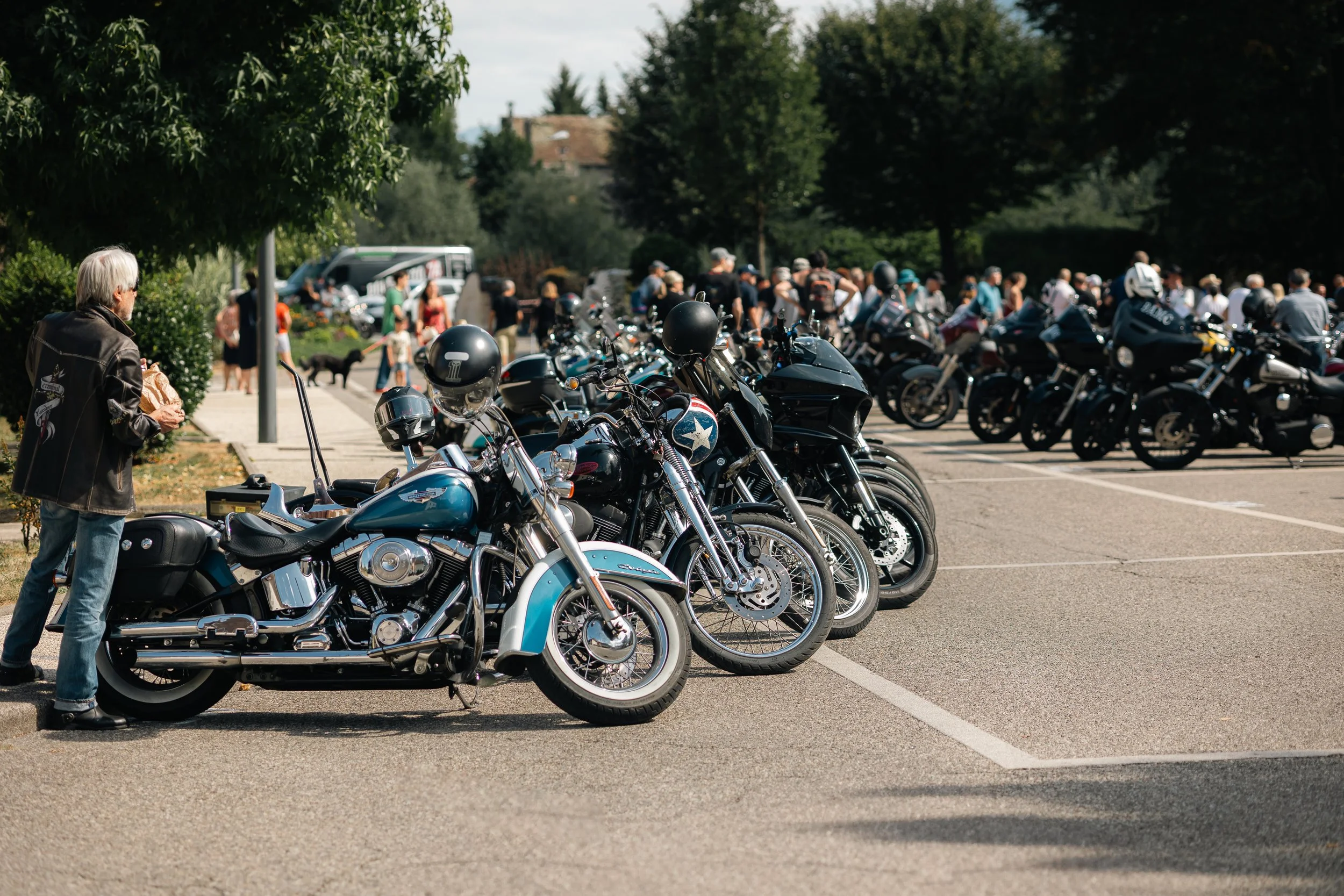 Rangée de motos et un homme près d'une moto, un rassemblement de motards, arbres en arrière-plan, jour ensoleillé.