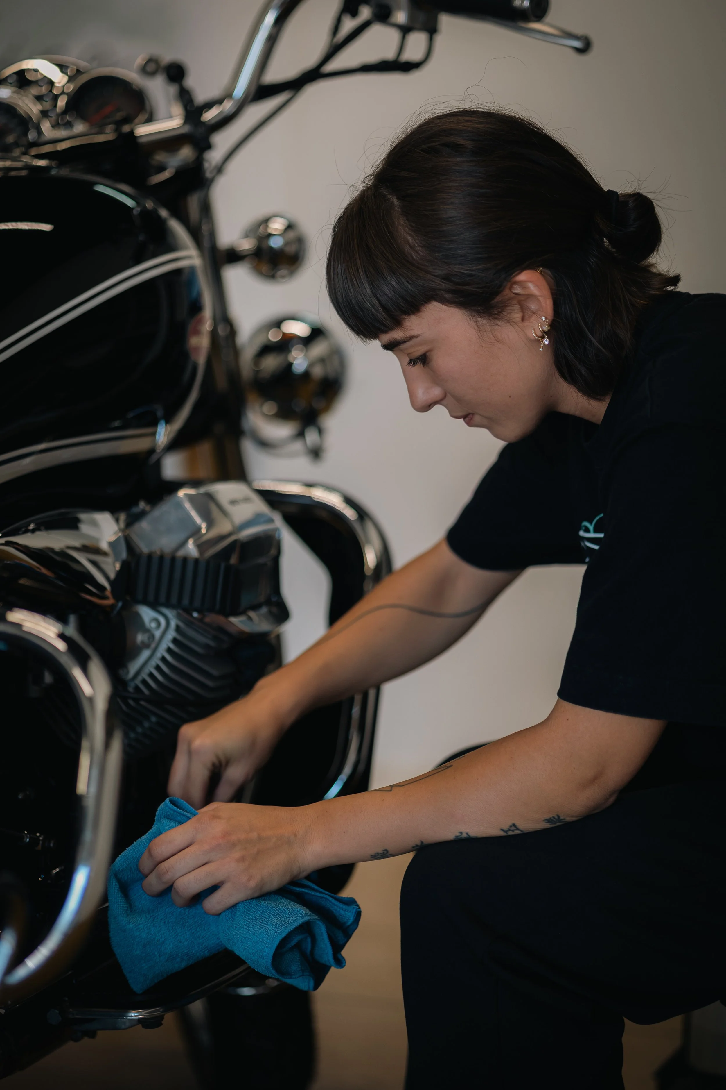 Une femme nettoie une moto noire avec une serviette bleue.