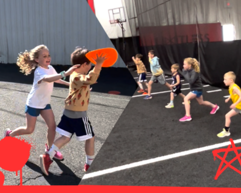 Children playing outdoors, with some running and others participating in a game involving a frisbee, on a sports court with basketball hoops.