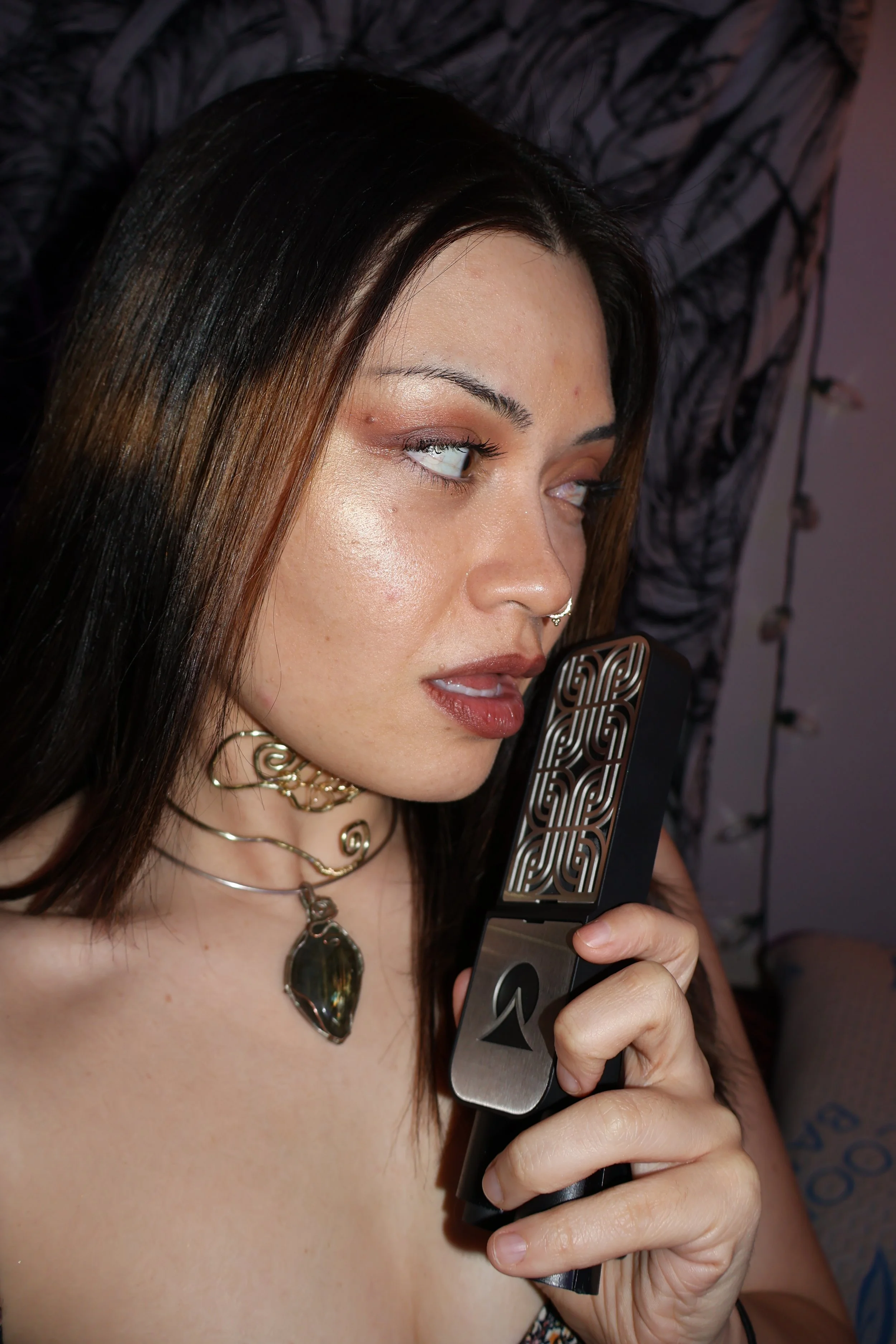 A woman with dark brown hair and light skin holding a retro style electric shaver, with a black and white patterned background.