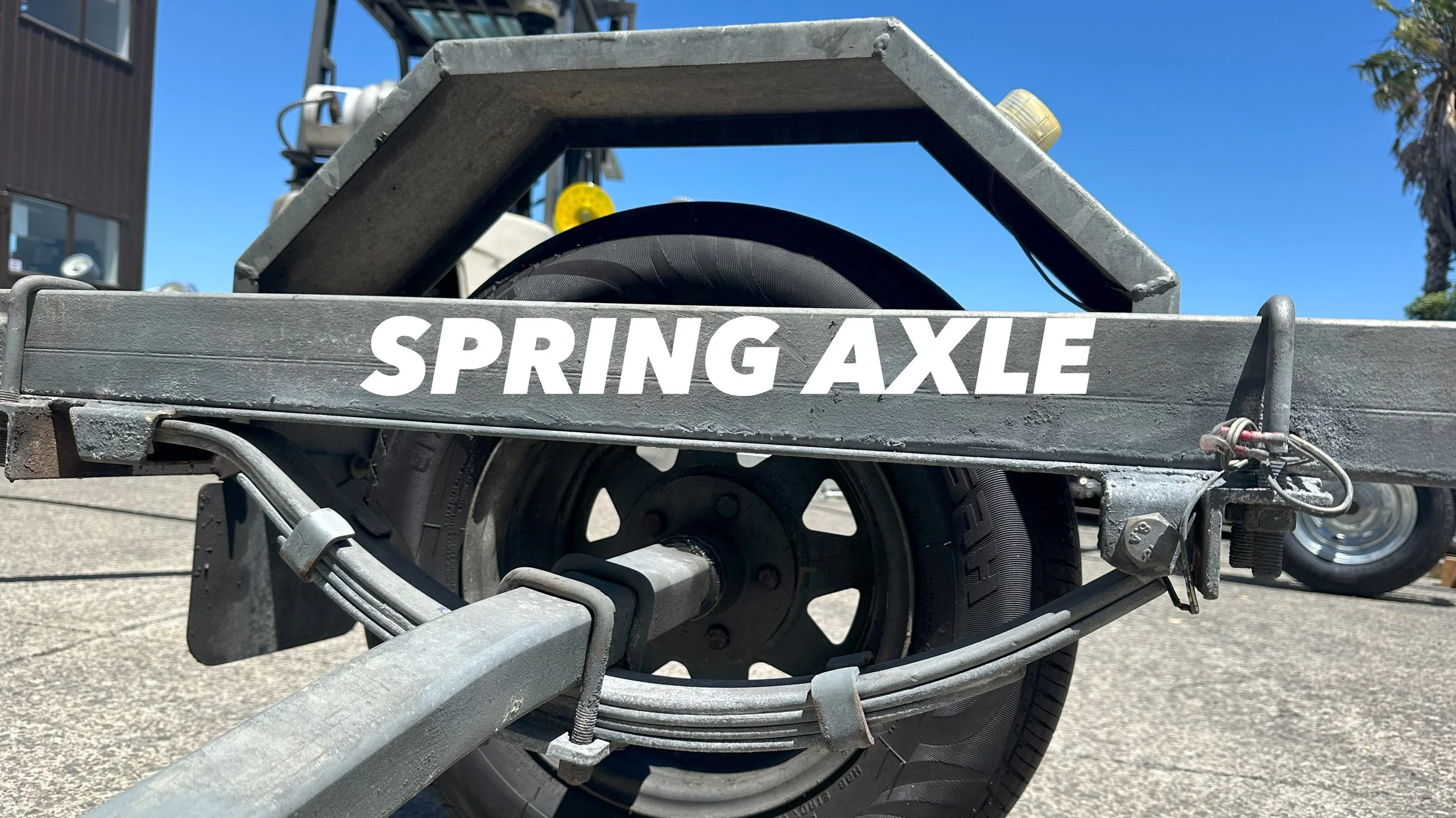 Close-up of a boat trailer with a sign that reads 'Spring Axle' attached to the axle near the wheel, with clear sky in the background