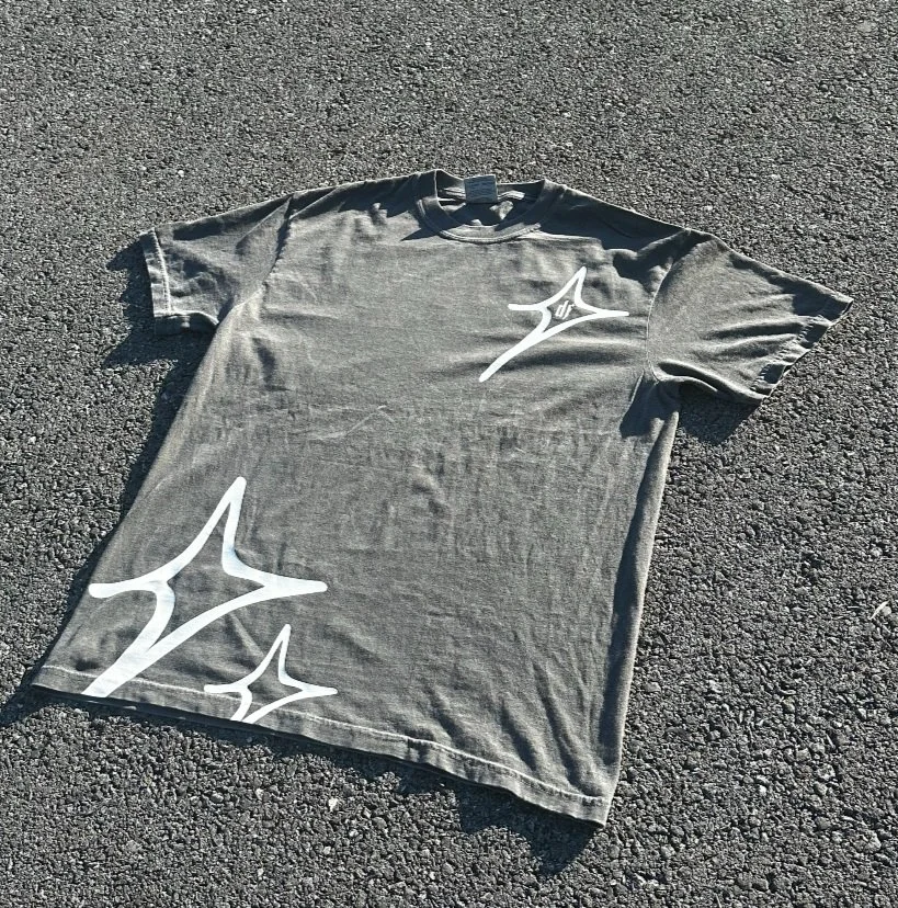 Gray tee with white star graphics laid on pavement