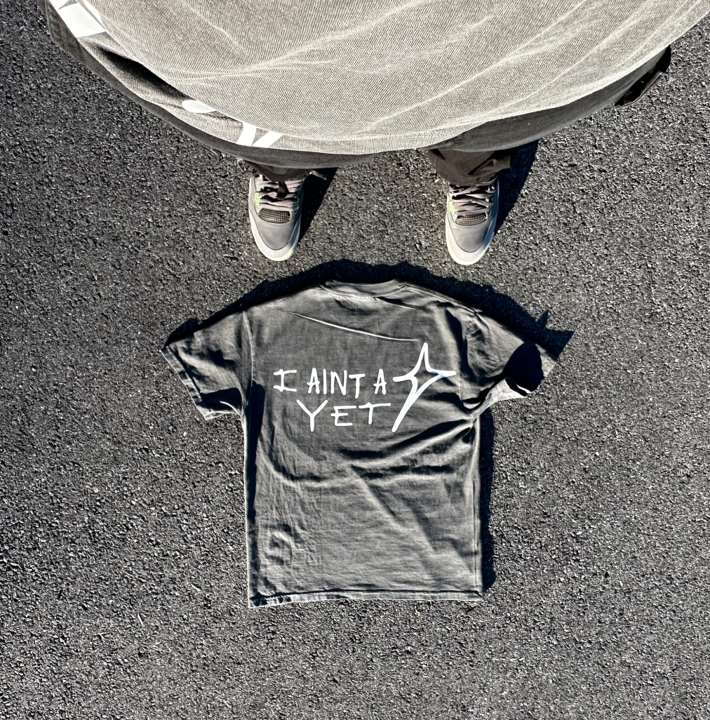 Gray tee printed with "I ain't a star yet" laid on pavement