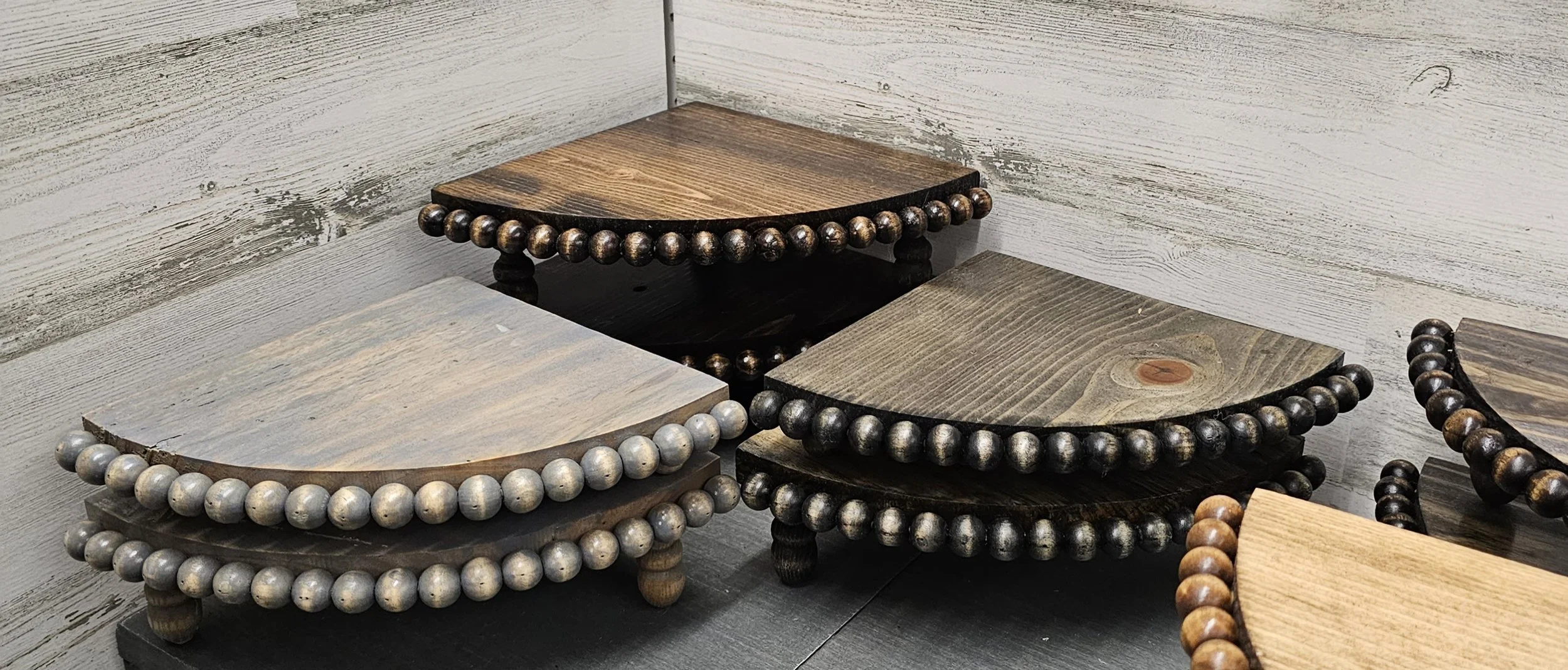 Close-up of several small wooden tables with bead trim along the edges, arranged against a white, weathered wood wall.