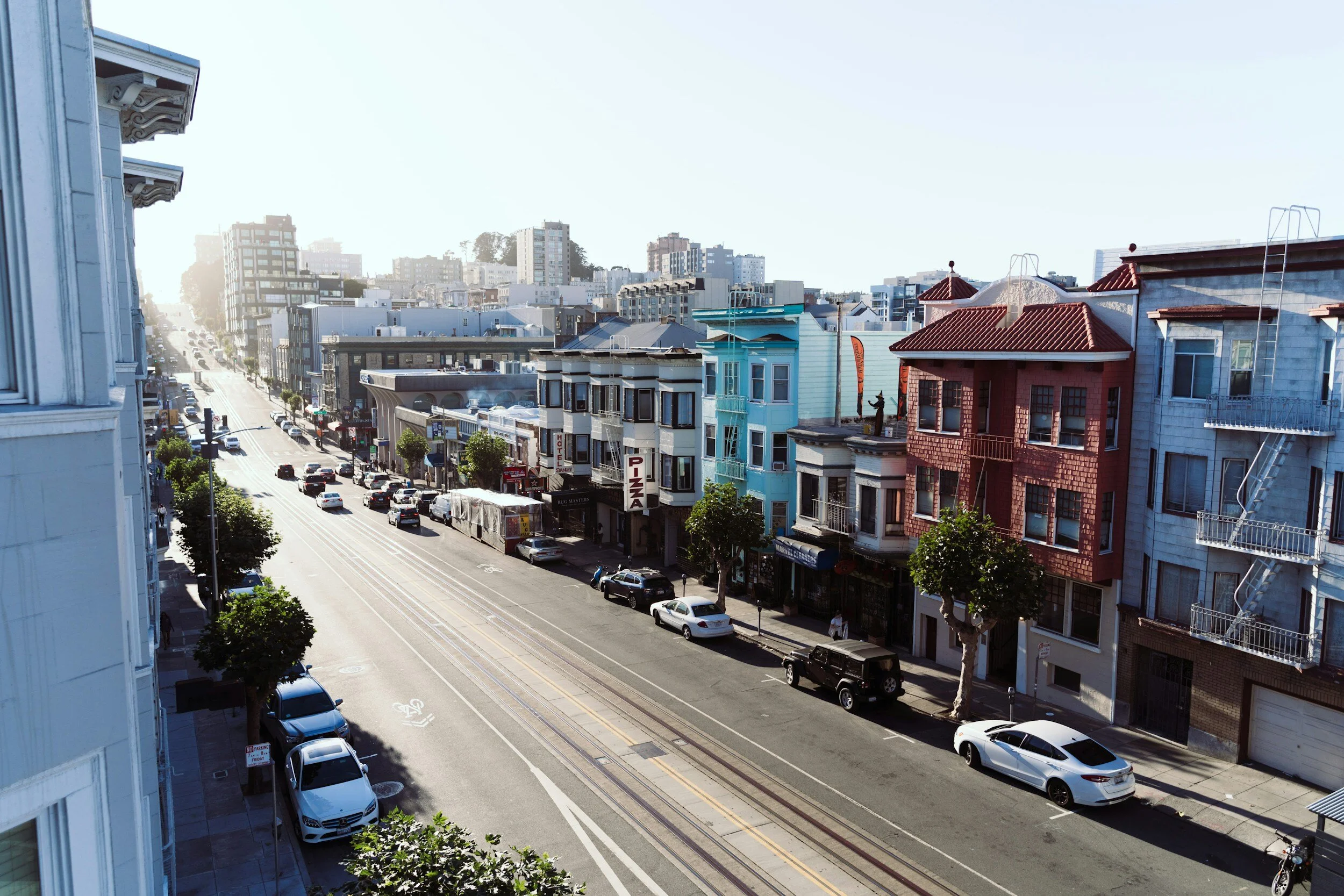 Street scene in an urban area with colorful buildings, parked cars, and light traffic.
