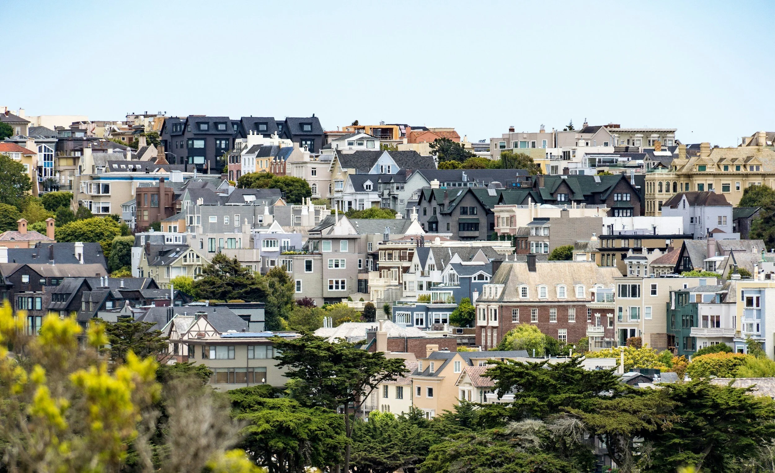 View of a densely packed hillside neighborhood with diverse architectural styles, featuring houses and trees.