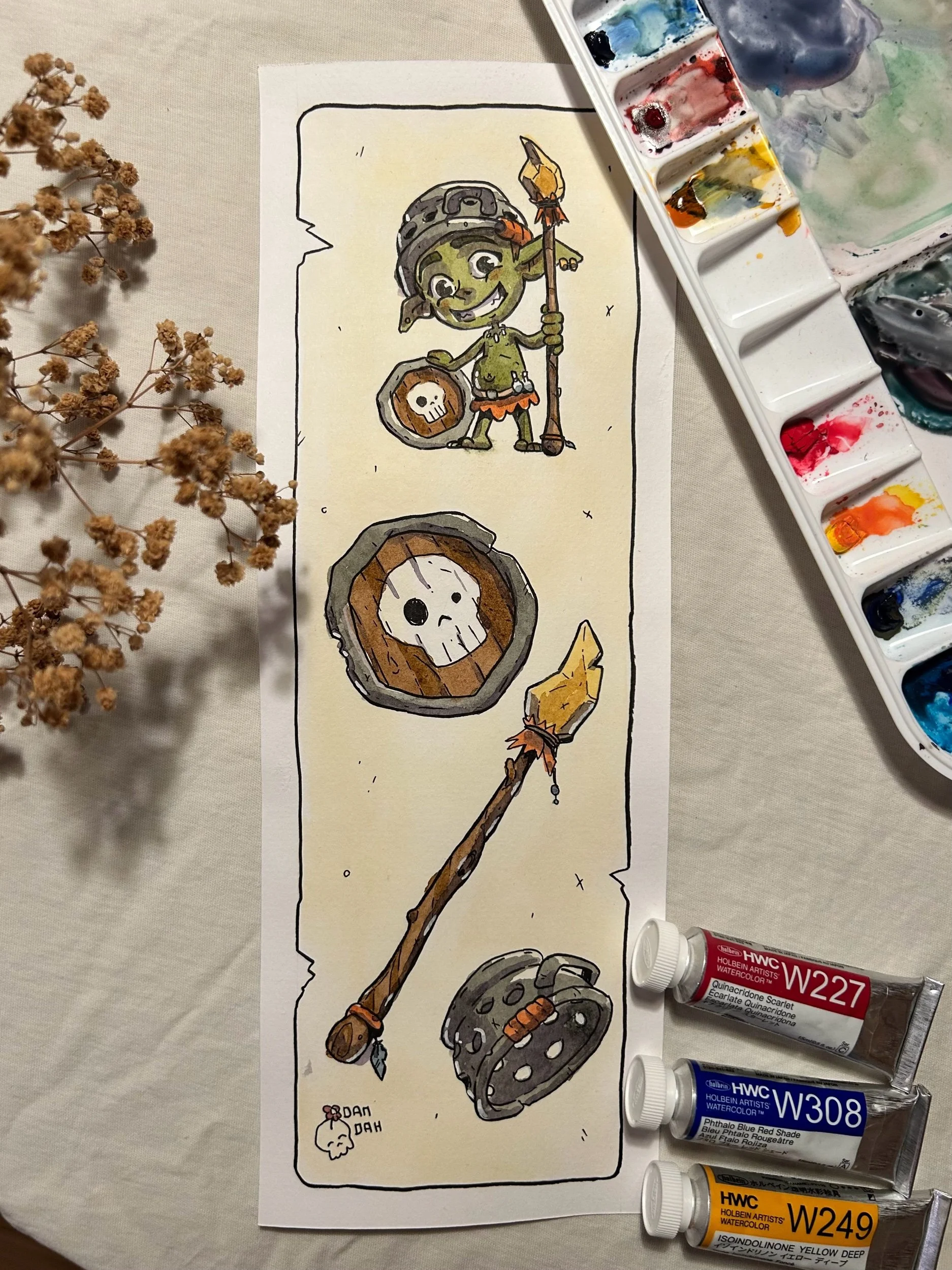 Green goblin with shield, spear and bracer, ink and watercolor illustration on paper beside a paint palette.