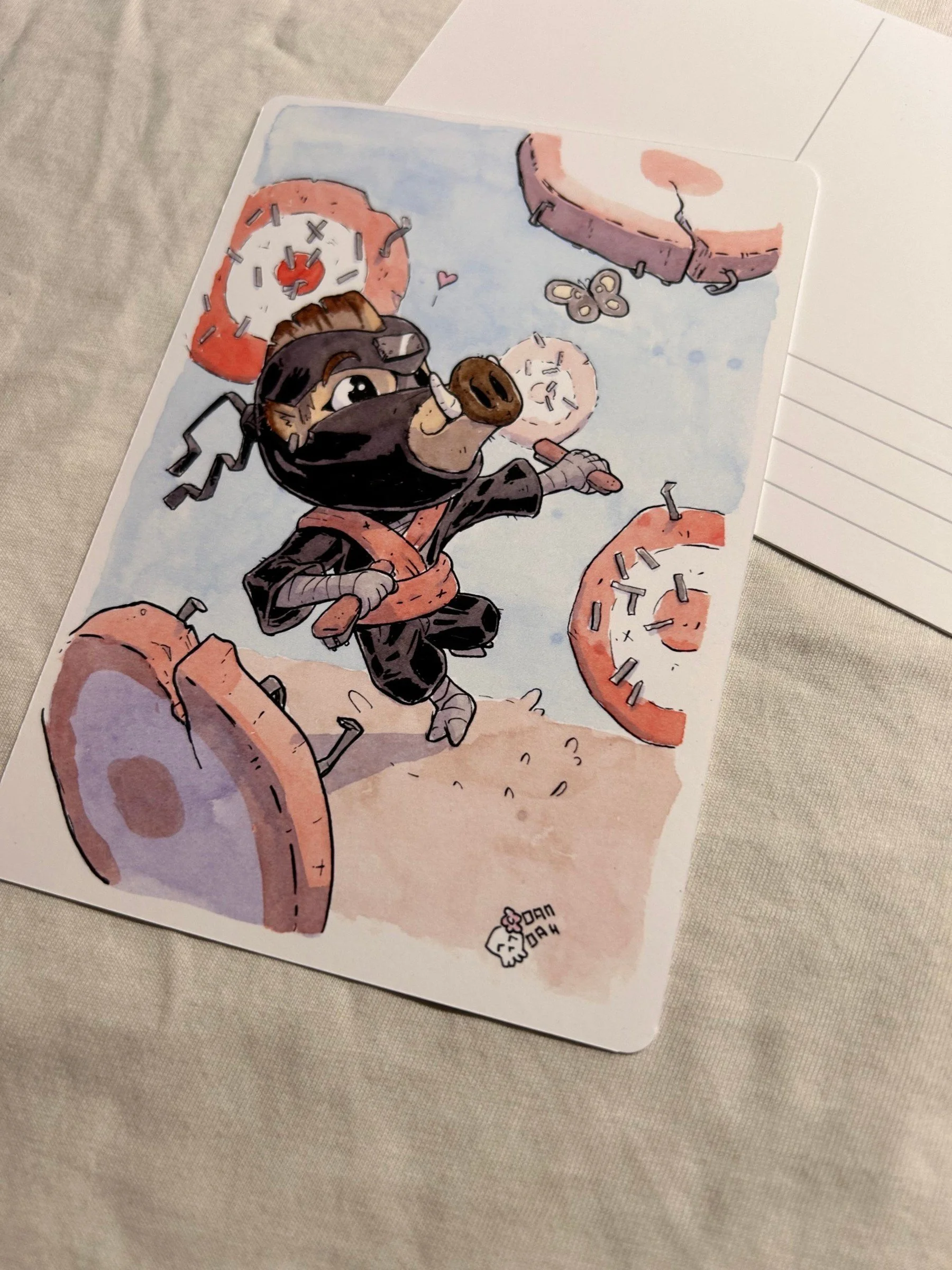 Angled view of the wild boar ninja postcard with cracked targets and staples, ink and watercolor illustration.