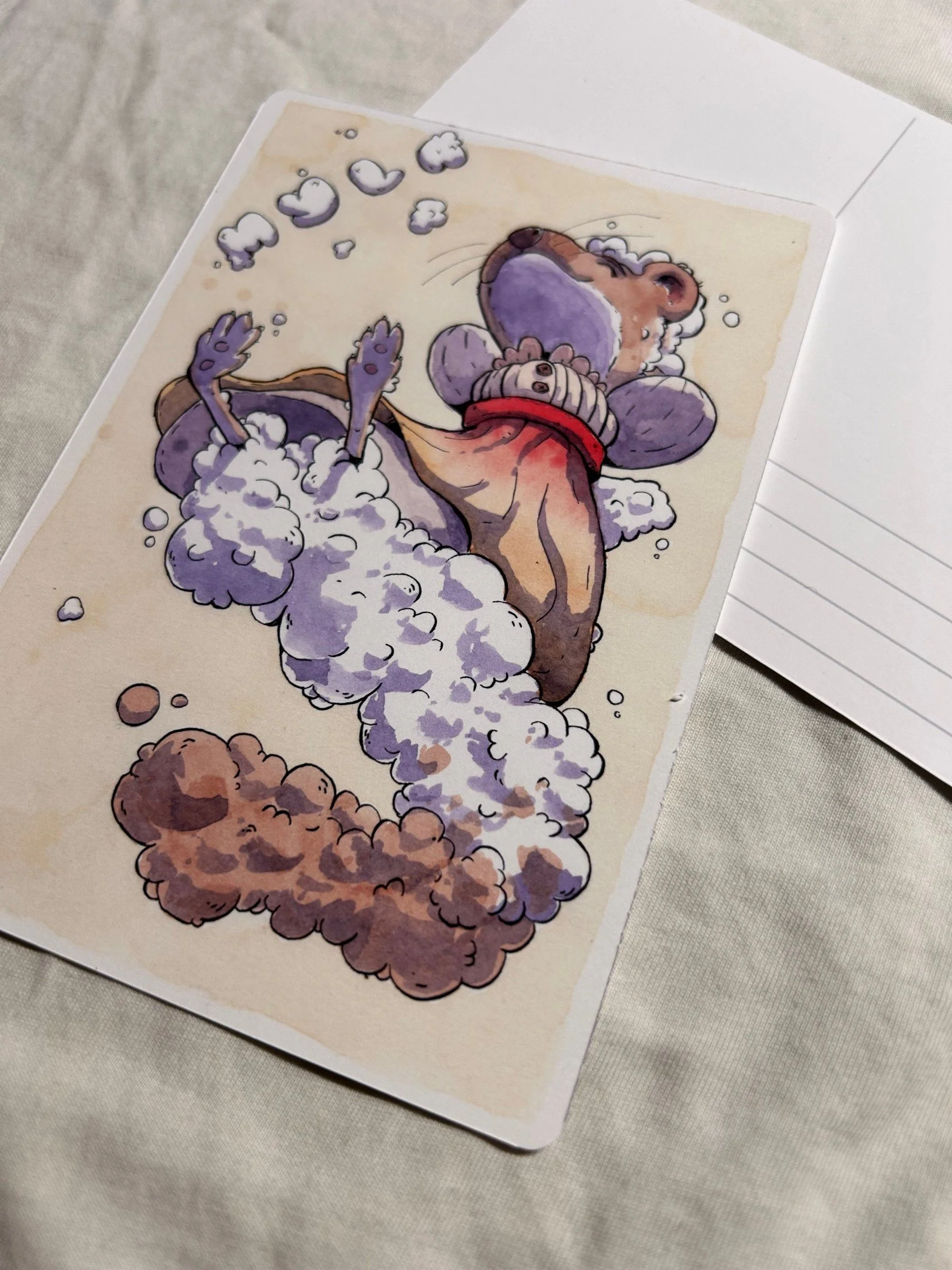 Angled view of the weasel postcard showing cloud tail and warm paper tones, ink and watercolor illustration.