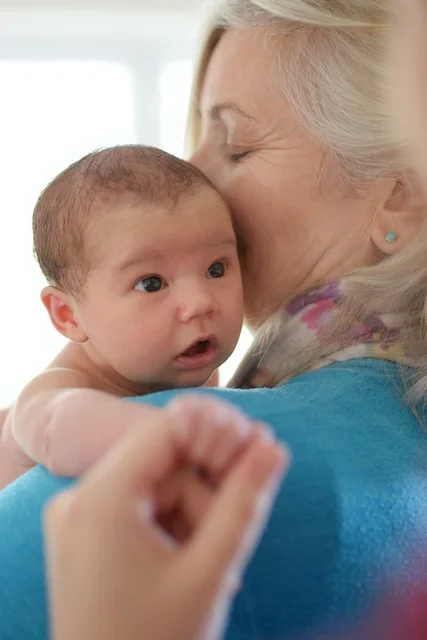 Image of Annie Barber facing away from the camera, she has her eyes closed and is holding a baby that she has just bathed, the baby has her eyes open wide and is looking towards her mother, just out of shot.