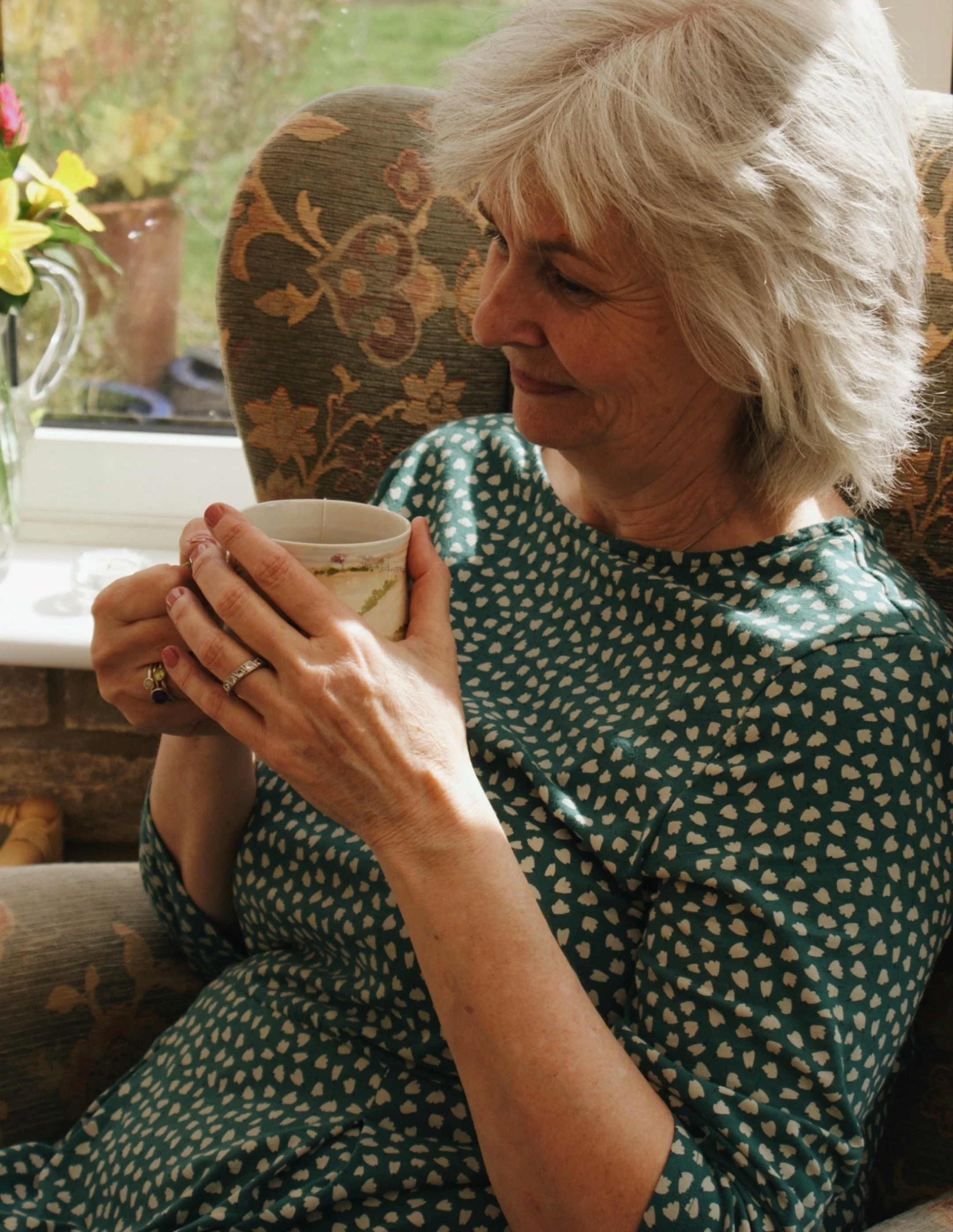 Annie Barber sitting in with mug of tea in her hand, she is sat in a relaxed position, listening to a client.