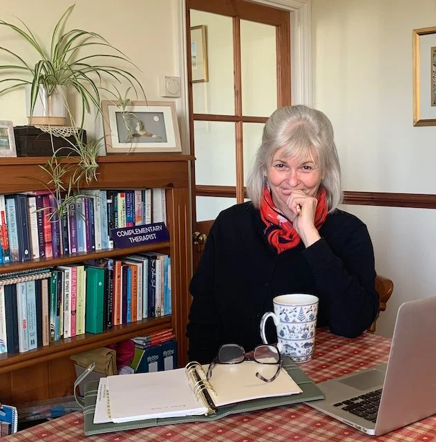 Annie Barber in the office, looking towards camera with her laptop, notebook and mug of tea at the ready -