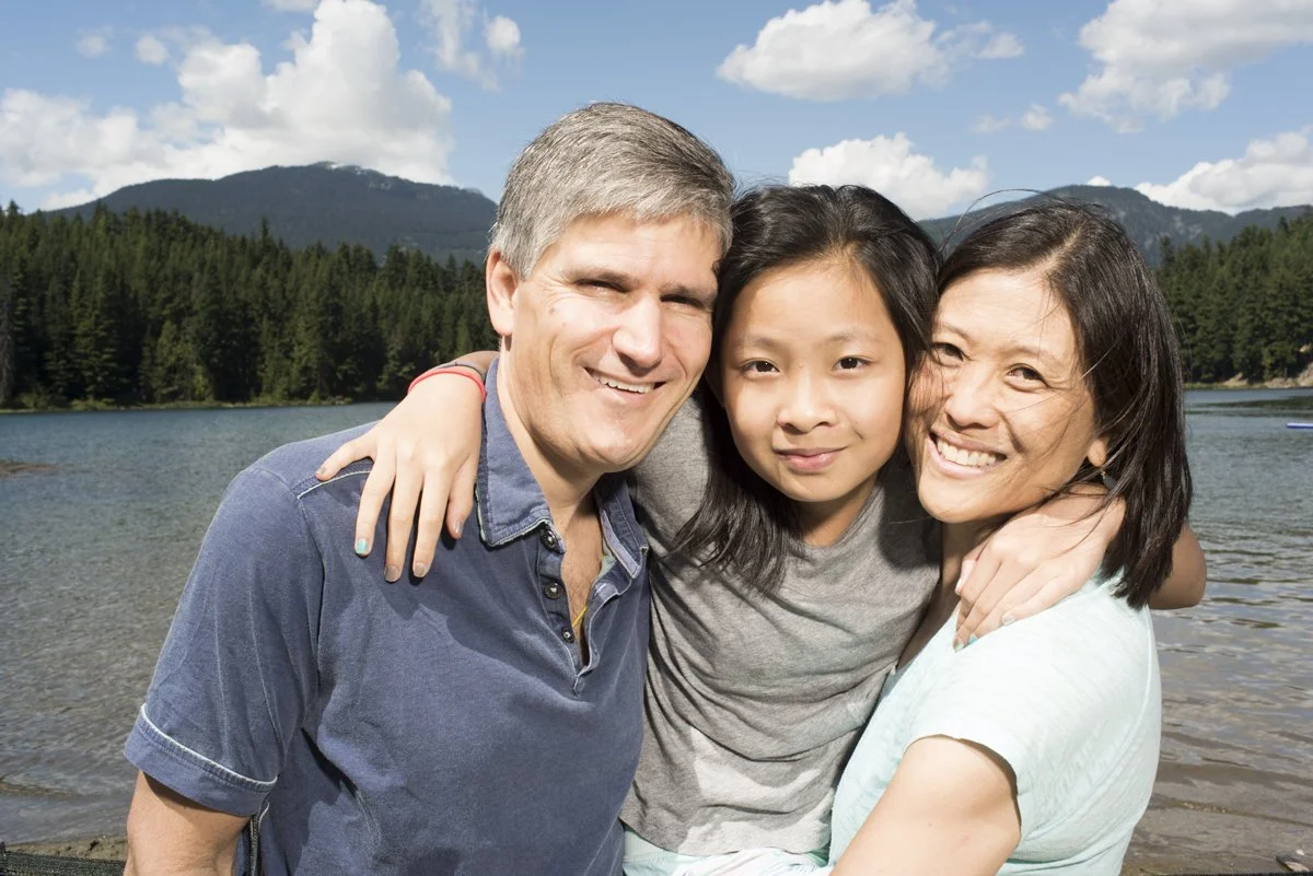Mom, dad and little girl embrace by a glacial lake in Whistler.